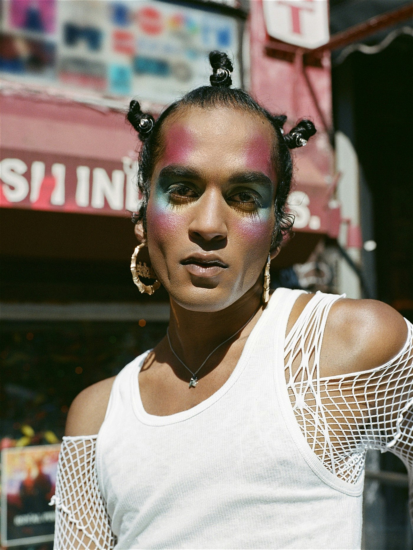 A Black male wearing make up, large hoop earrings and an off-the-shoulder white top