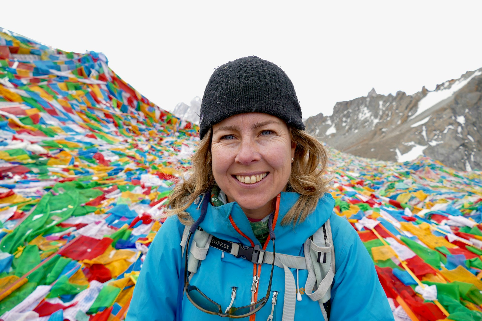 A selfie of a woman on a mountaintop surrounded by colorful prayer flags