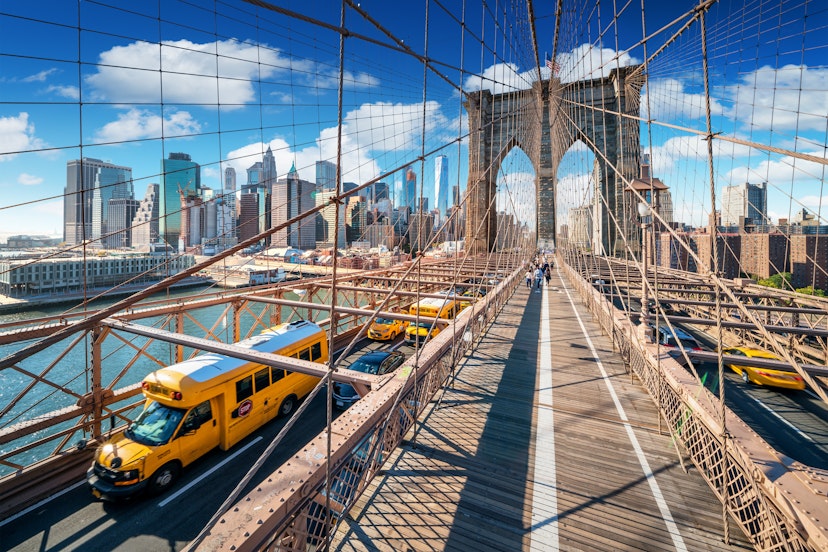 Traffic (with yellow taxis) and pedestrians cross Brooklyn Bridge on a sunny day.