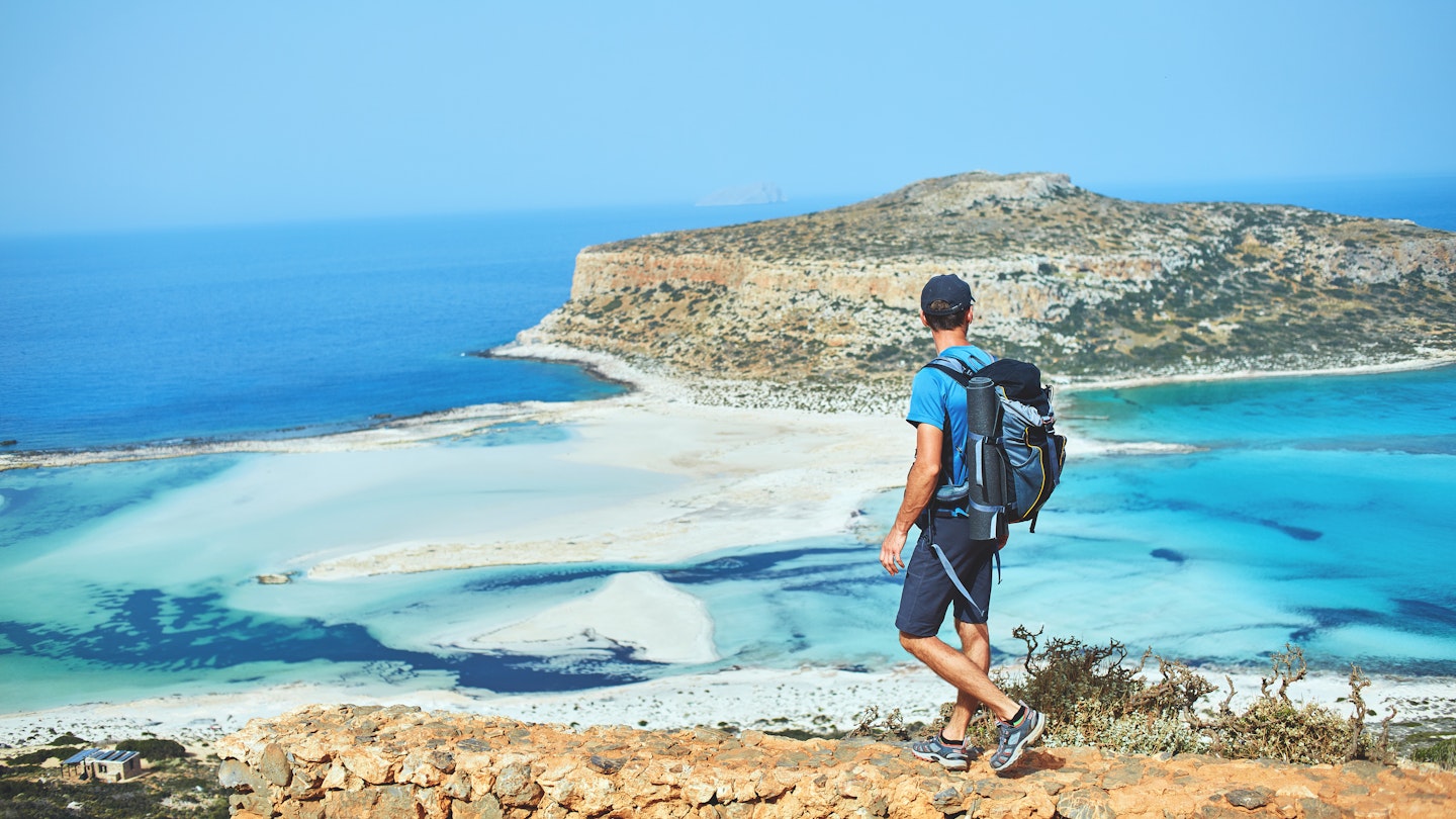 back view of hiker with small backpack on the trail to the Balos beach at early morning. Balos beach on background, Crete, Greece