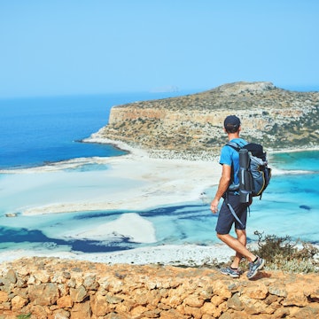 back view of hiker with small backpack on the trail to the Balos beach at early morning. Balos beach on background, Crete, Greece