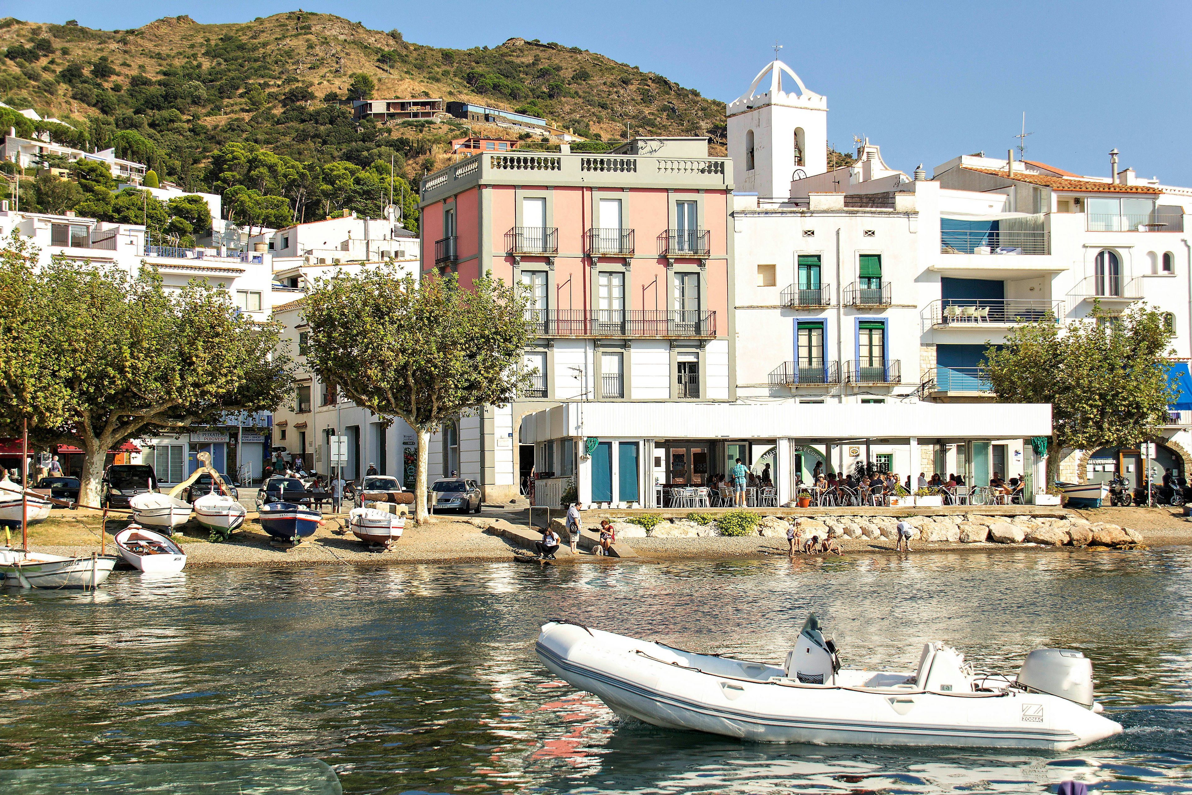 Houses and apartment buildings line a waterfront. A small white boat is anchored in the foreground