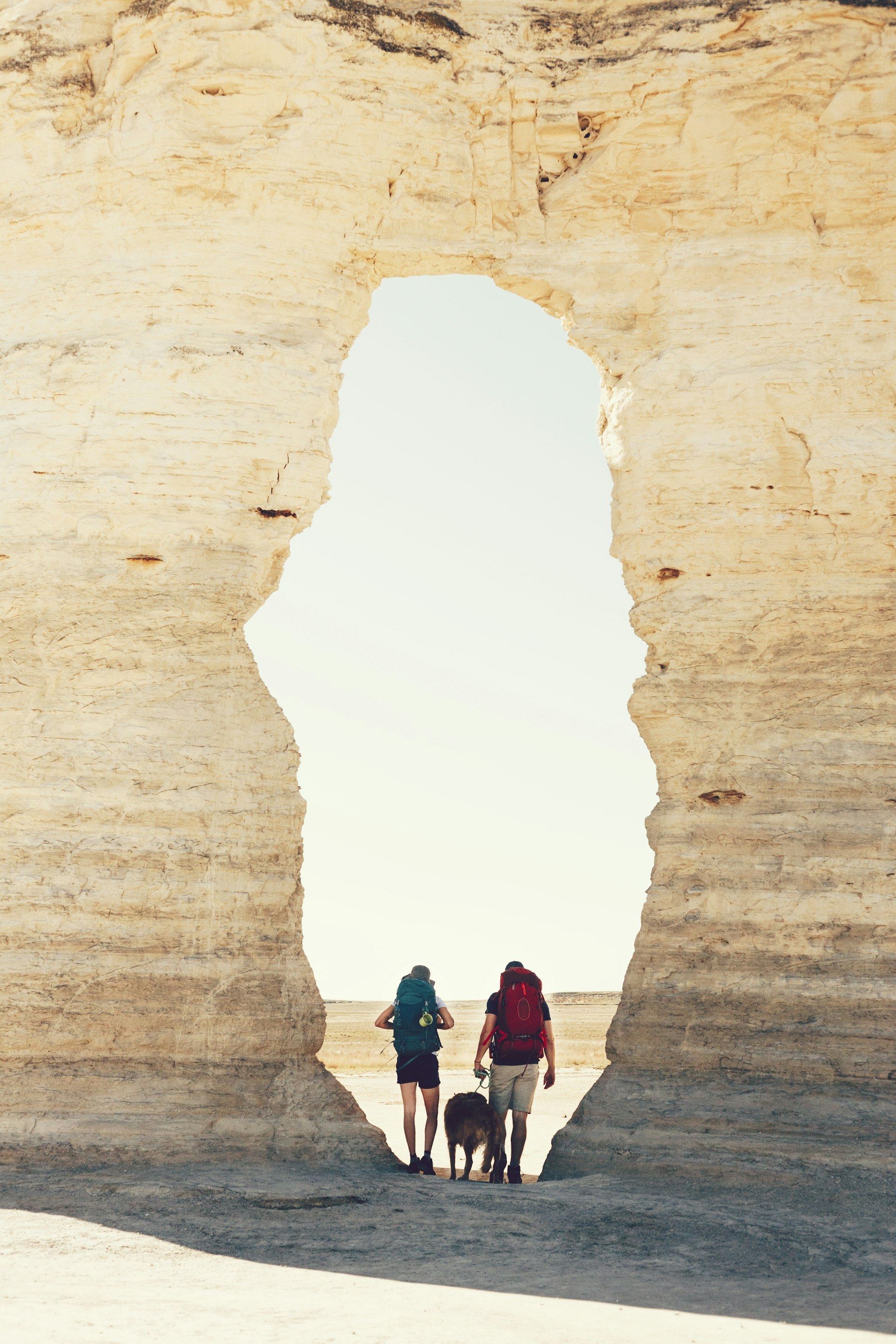 Two hikers and a dog are framed by a natural stone archway  