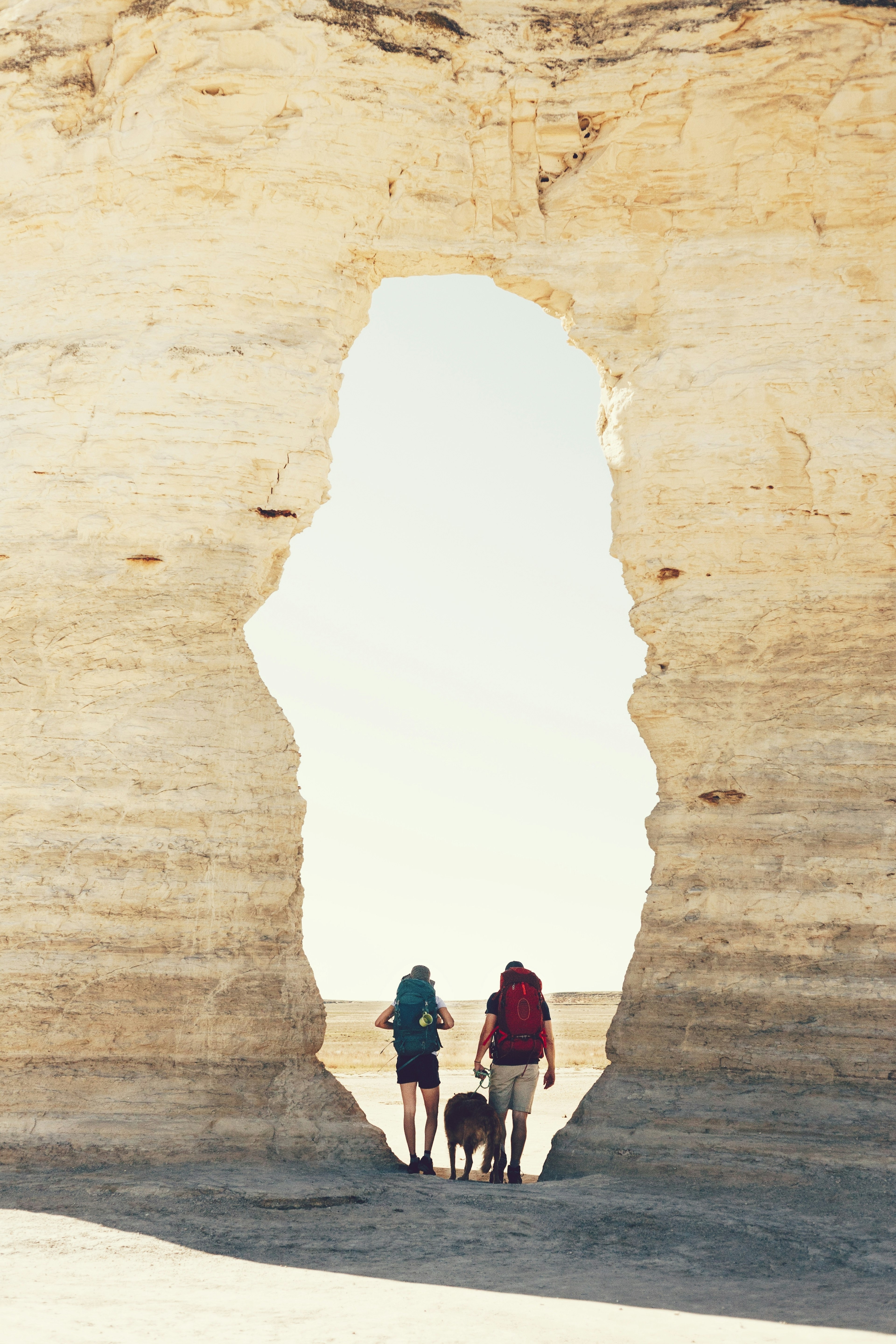 Two hikers and a dog are framed by a natural stone archway