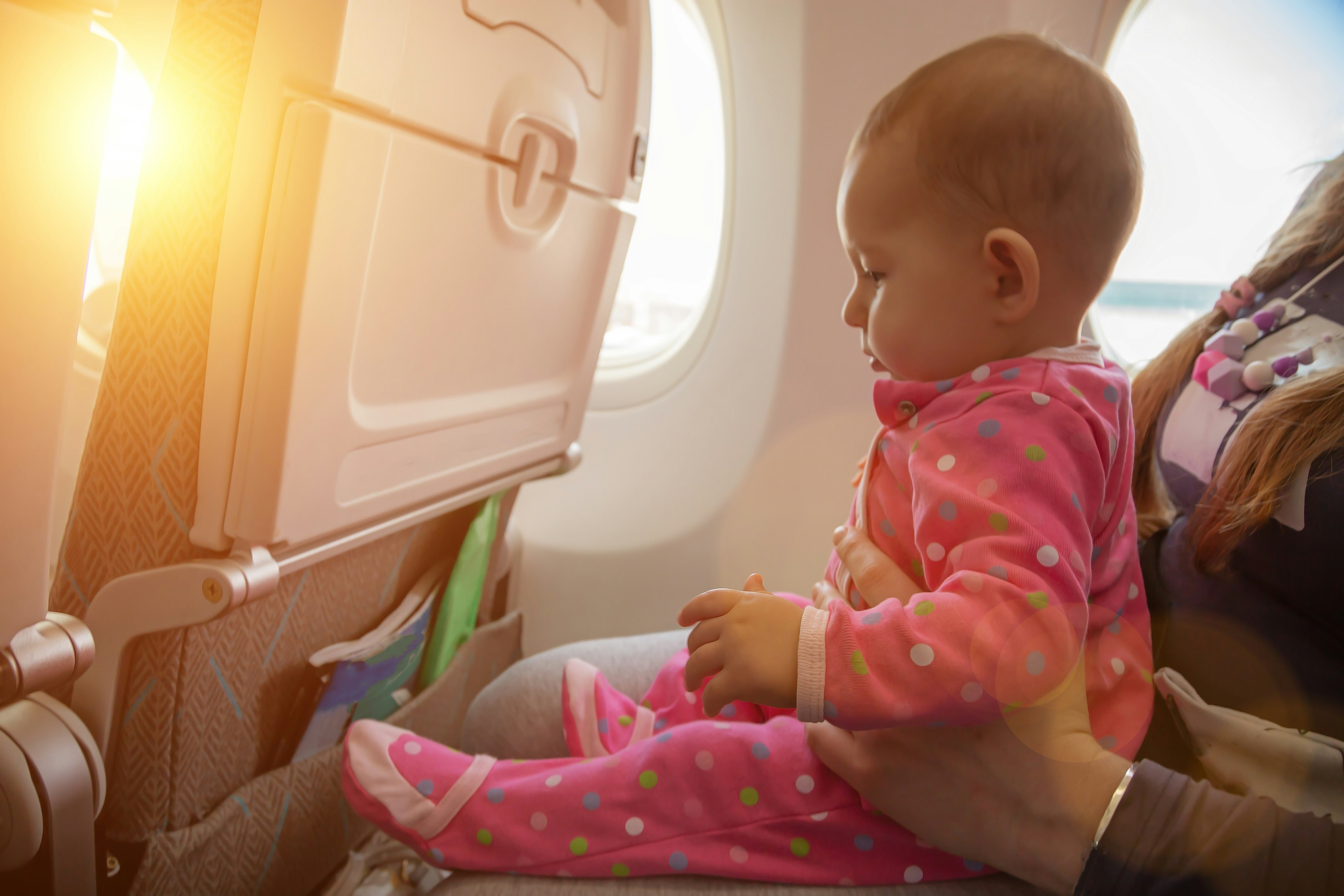 Mother holding a baby on her lap near an airplane window on a sunny day