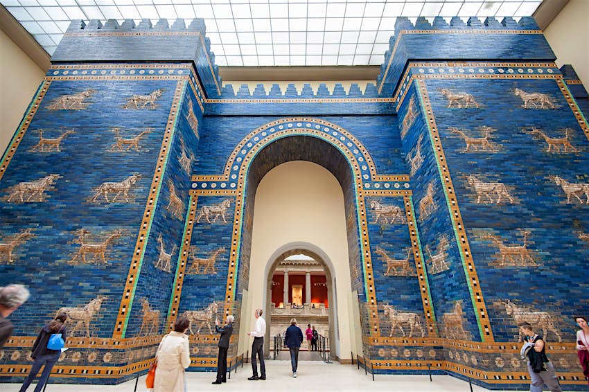 Les visiteurs marchent ou se tiennent devant les murs bleu vif de la ville babylonienne à l'intérieur du musée de Pergame.