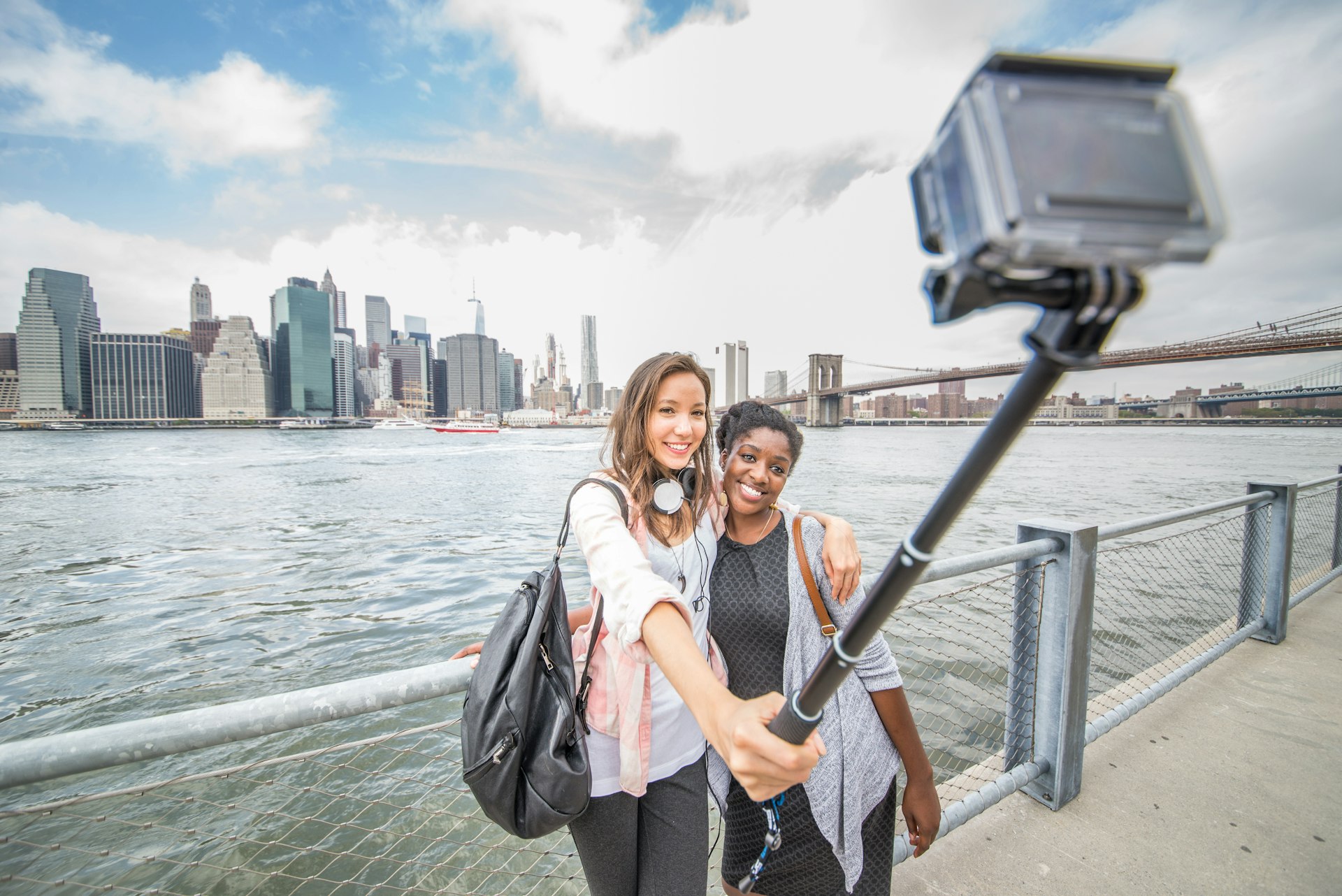 Two women taking a selfie with Manhattan and Brooklyn Bridge in the background. 