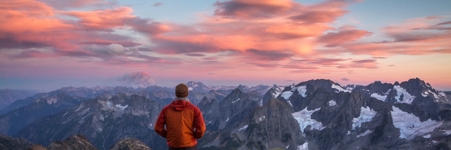 Hiker stands at his mountain top camp during sunset in North Cascades National Park.