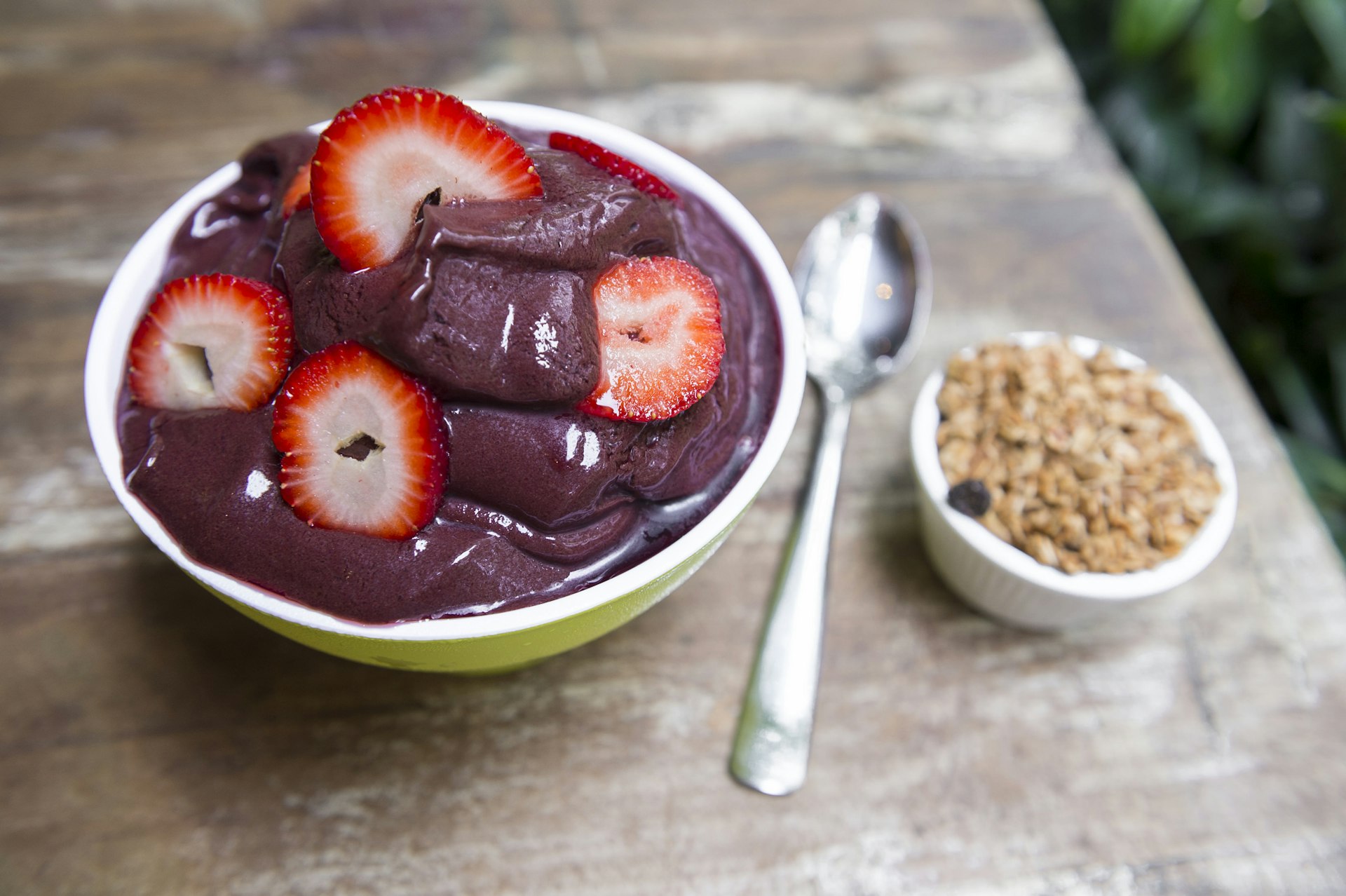 Bowl of fresh Brazilian acai garnished with strawberries and granola on a rustic wood table in Rio de Janeiro