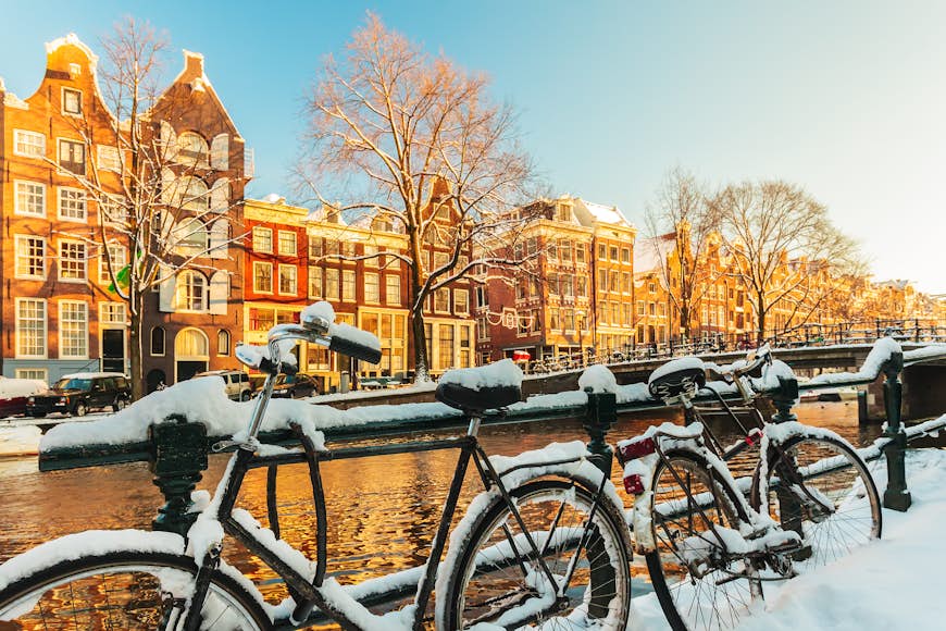 Bicycles covered with snow in front of a canal during winter in Amsterdam