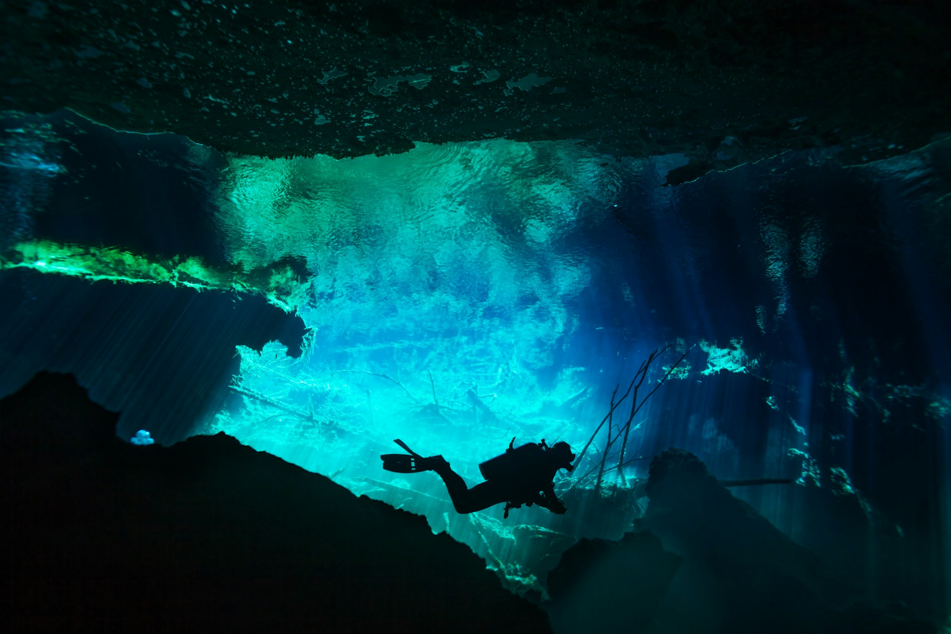 A scuba diver is silhouetted as they swim through blue water of a cave