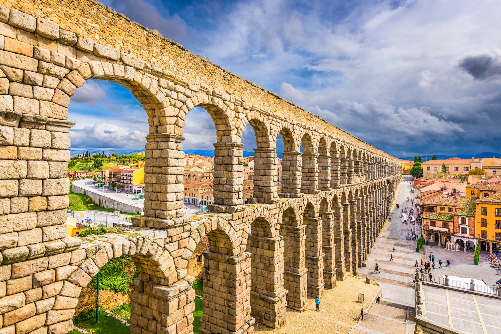 Sandstone-colored tall aqueduct lining a city square 