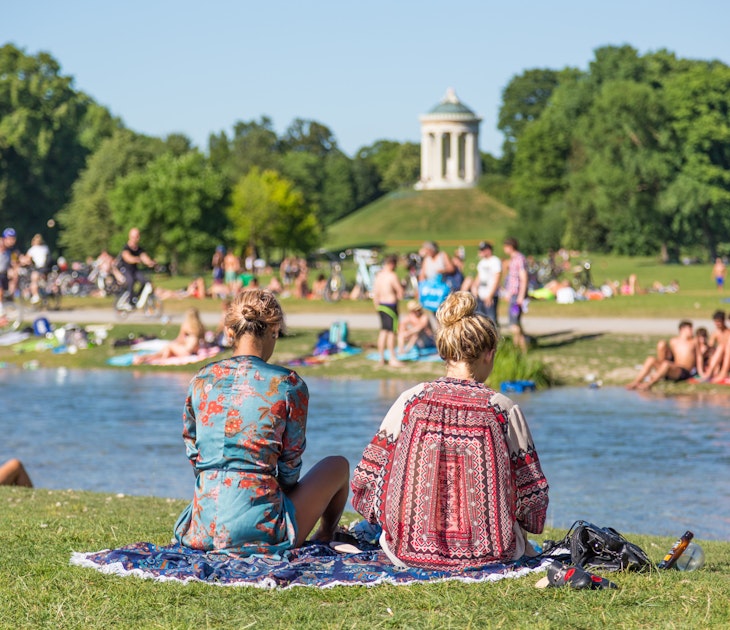 Two girls sitting on a rug at English Garden (Englischer Garten) with a crowd of others in the background.