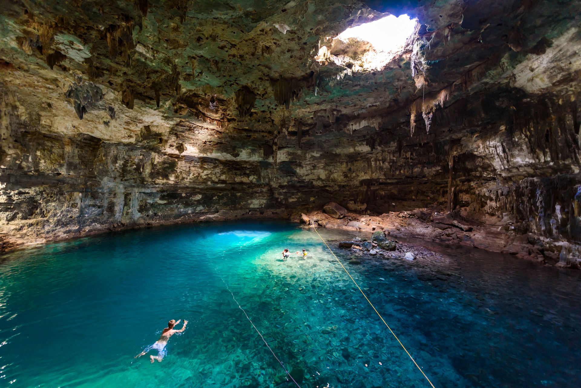 A swimming hole in a cave with a single light source coming from the hole in the cave roof