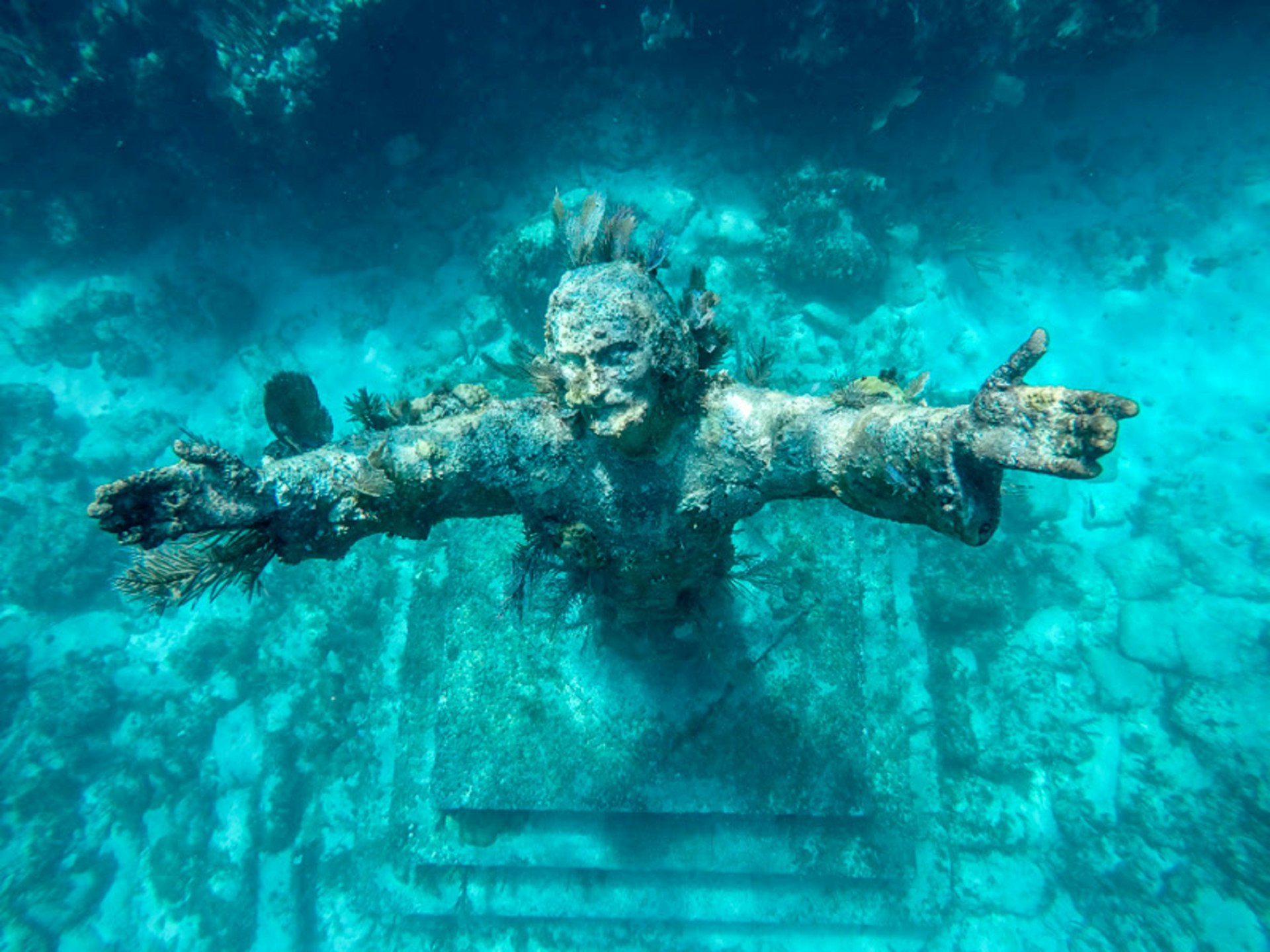 An underwater statue of a man with his arms raised towards the camera