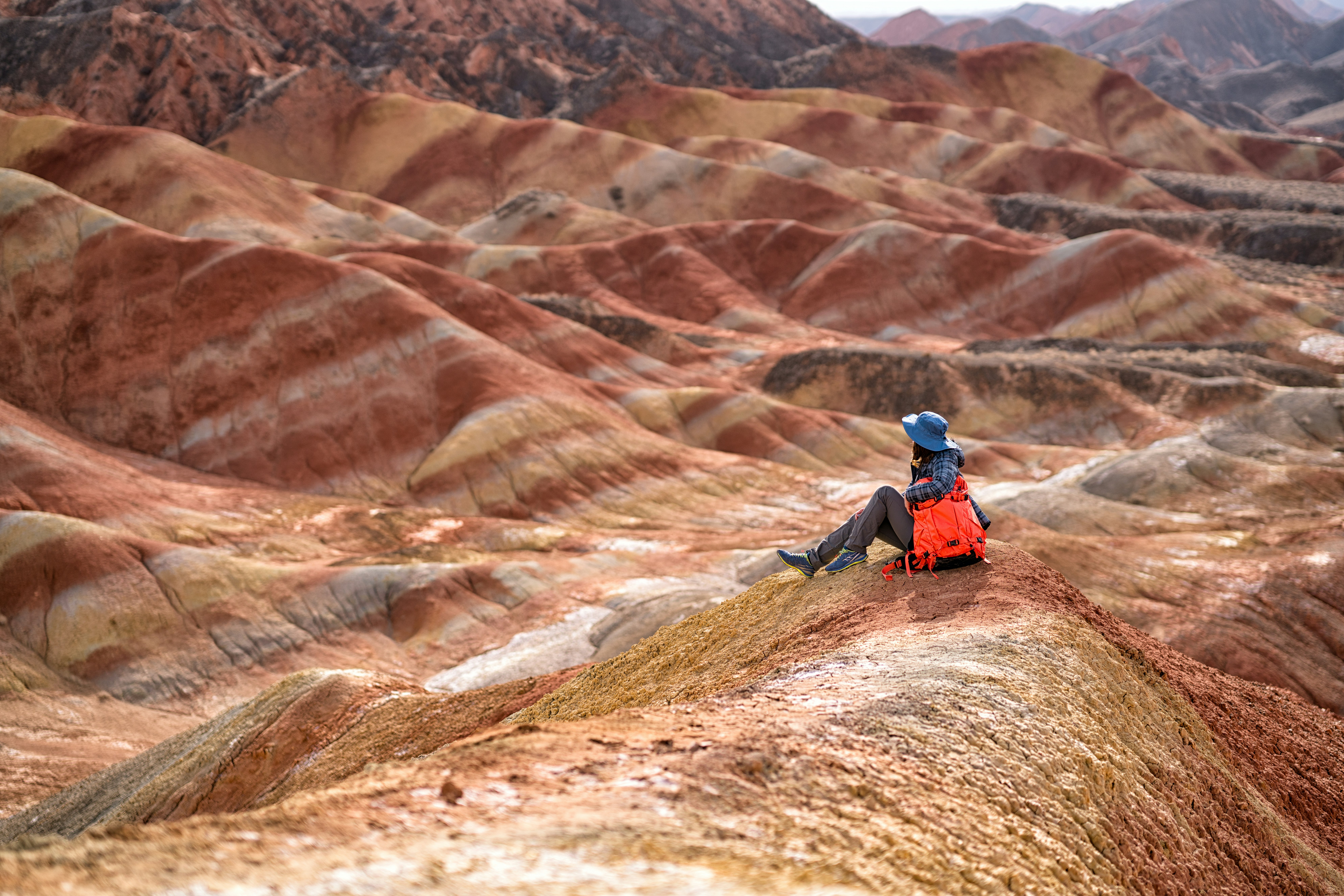 An adventure traveler sitting by an ochre-striped mountain in Zhangye Danxia National Geopark