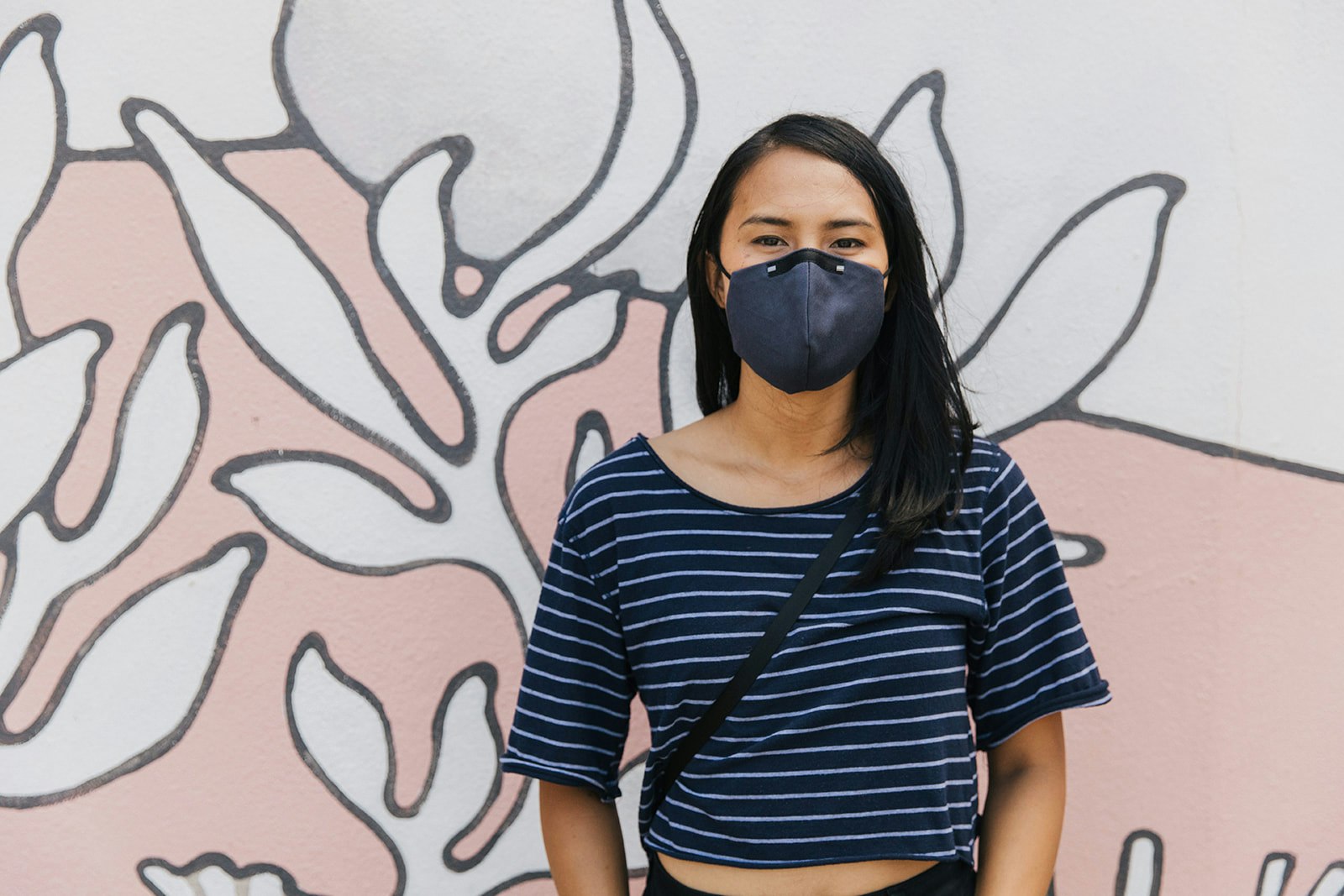 An Asian woman wearing a stylish navy face mask stands in front of a patterned screen
