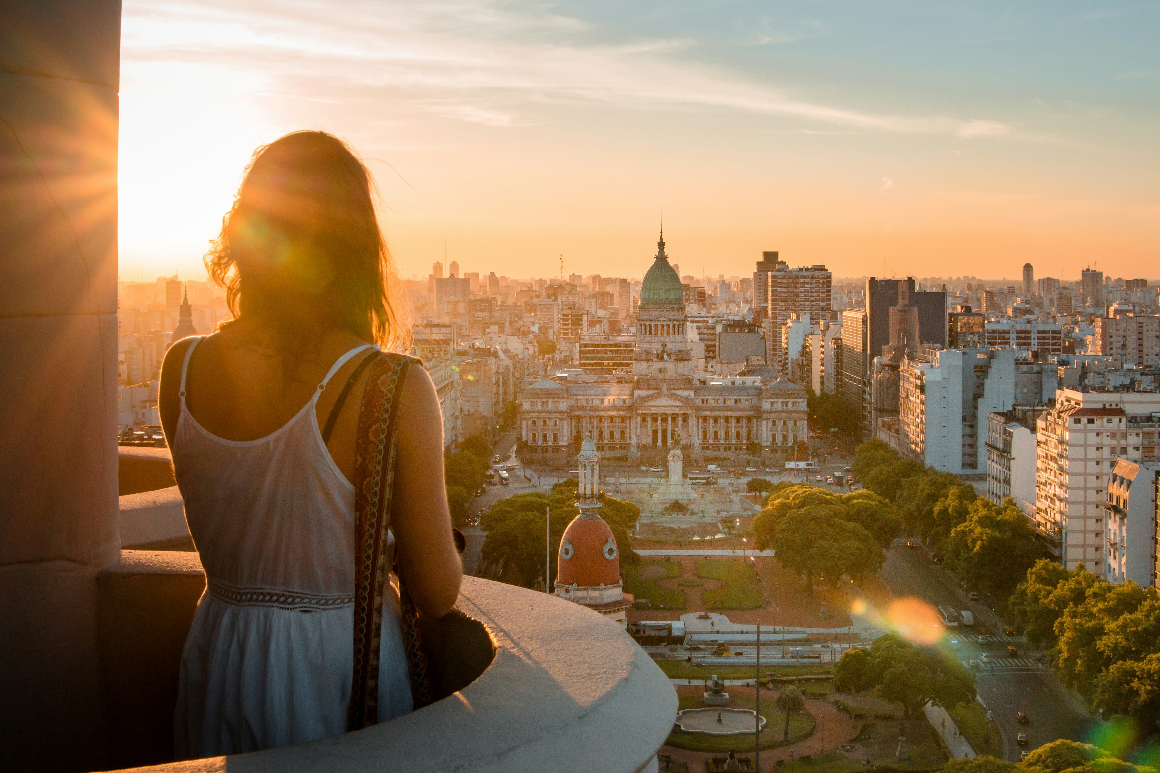 A woman standing on a balcony overlooking the Buenos Aires cityscape during sunset.
