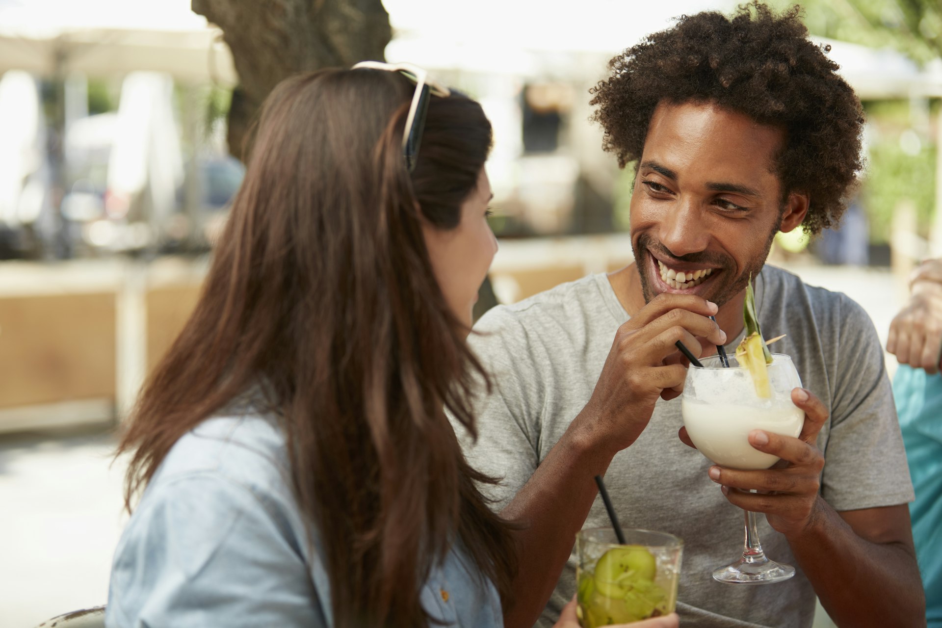 A Black man and a white woman laughing and smiling together as they have drinks at an outside bar