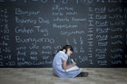 Schoolgirl sitting studying in front of large chalkboard with schoolwork chalked on it