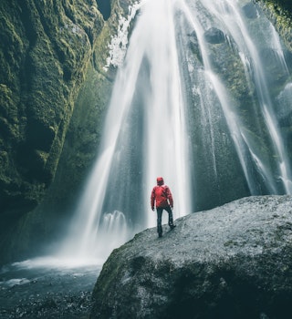 Person standing on a rock admiring Gljufrabui waterfall.