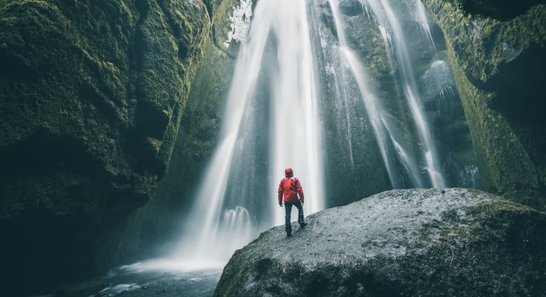Person standing on a rock admiring Gljufrabui waterfall.