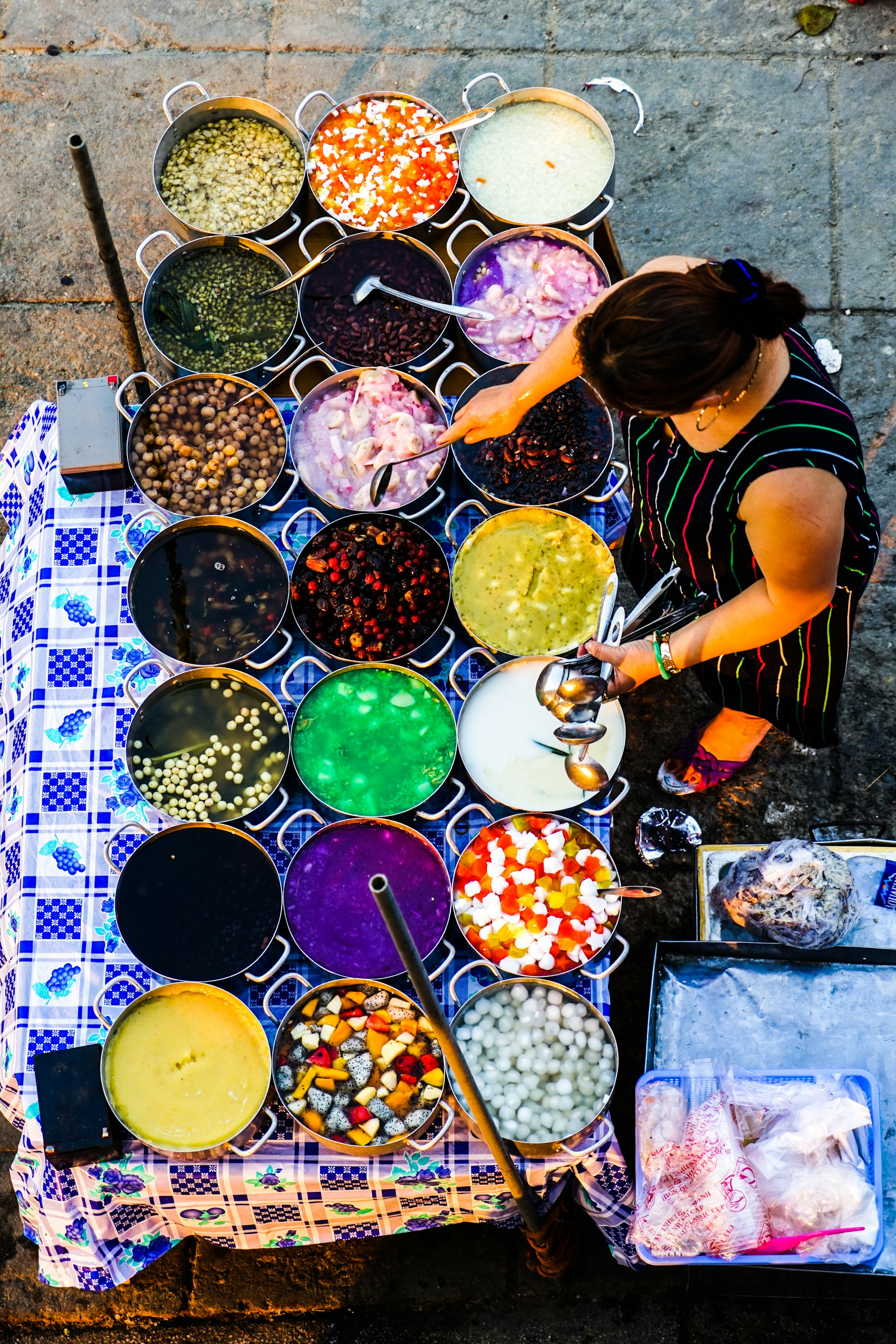 An aerial shot of a woman tending to a series of pots packed with colourful foods on a street food stall