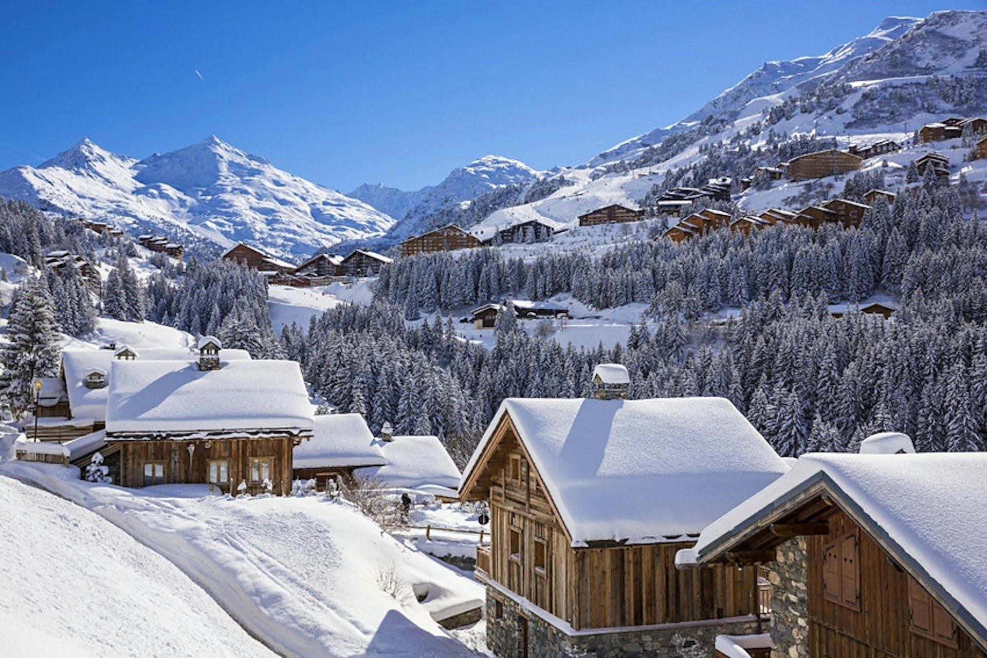 Snow covers roofs on a collection of small wooden cabins in Méribel