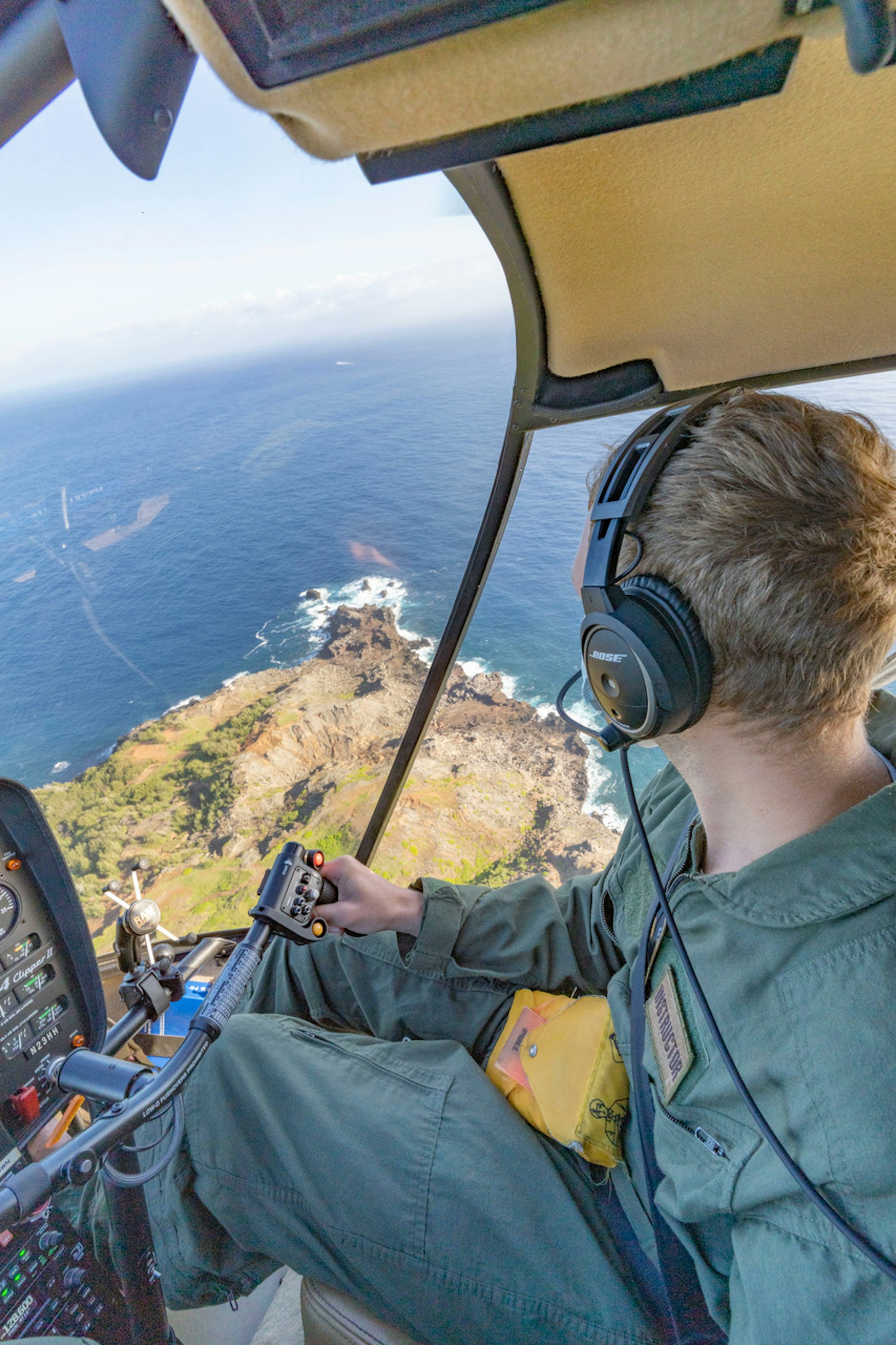 Inside the cockpit as a man flies a helicopter over a rocky coast