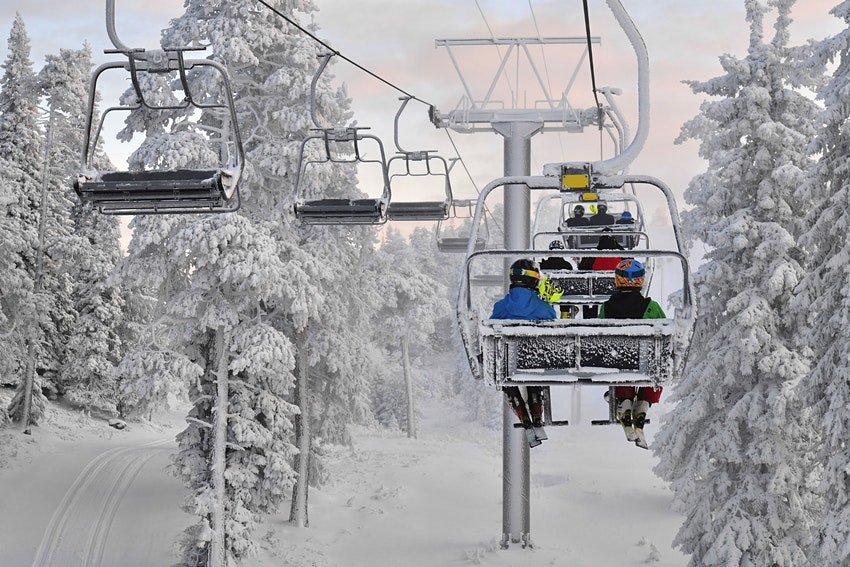 Skiers sit on a chairlift heading up a mountain flanked by snow-covered trees