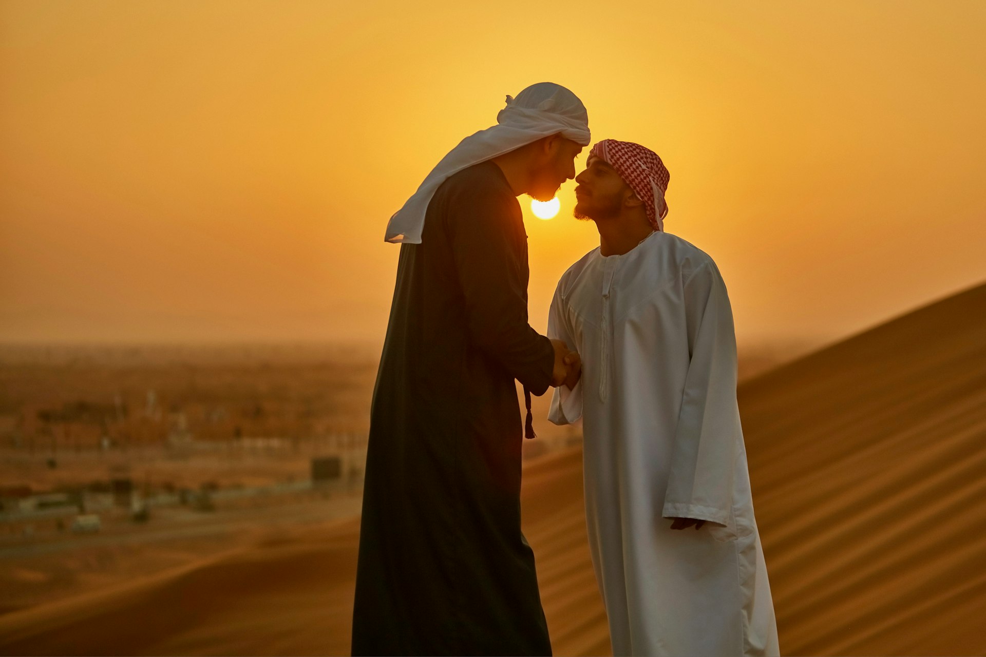 Middle Eastern men greeting each other with a handshake and nose rub in the desert at sunrise