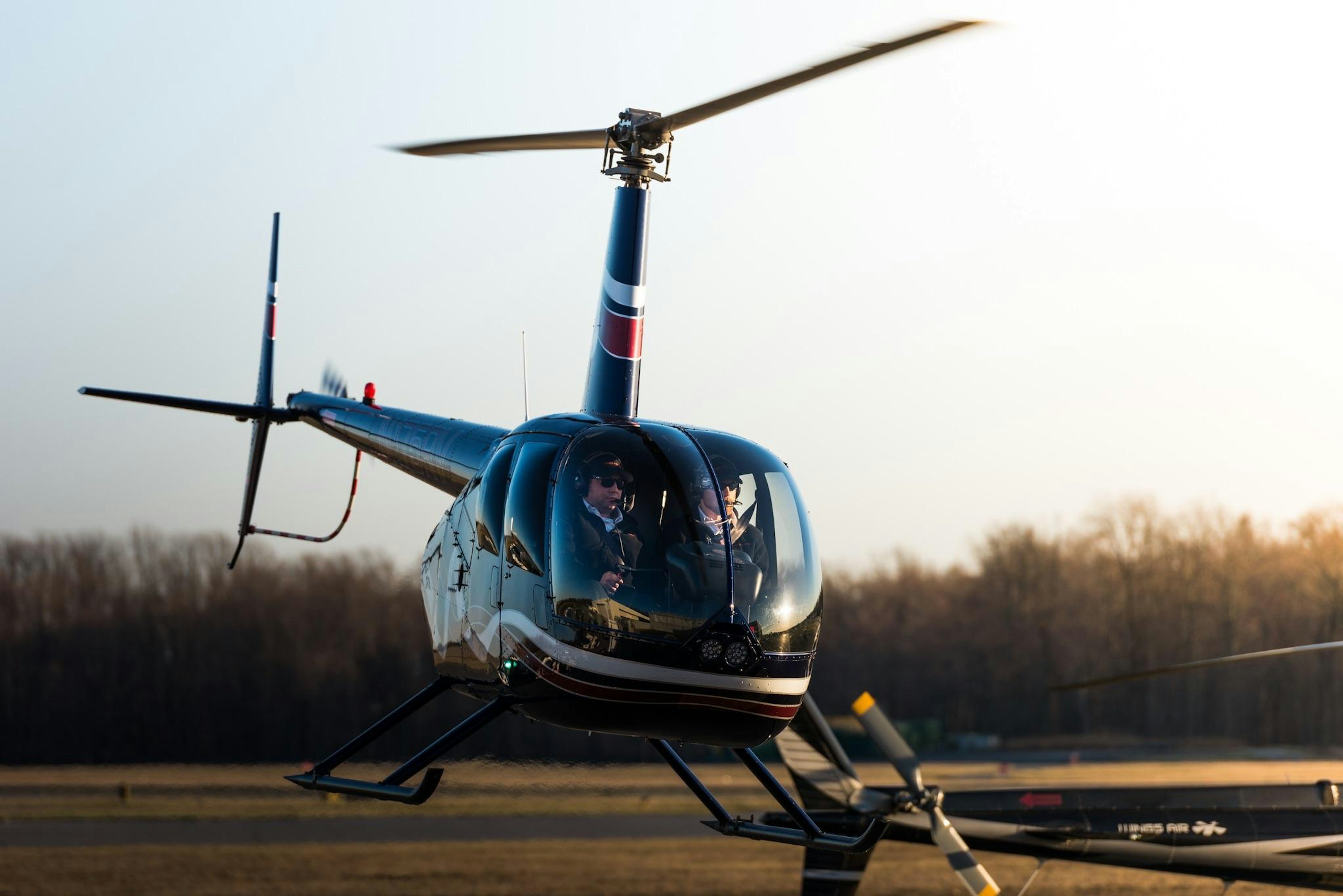 Two men fly a small helicopter low over the ground