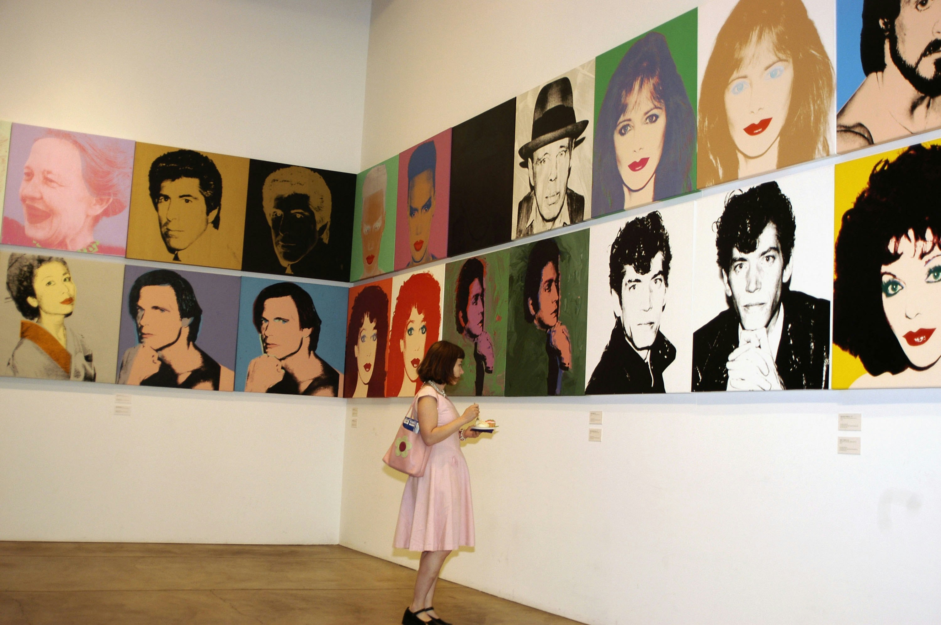 A woman stands in front of a display of multiple images of celebrities in bright colors at the Andy Warhol Museum in Pittsburgh. 