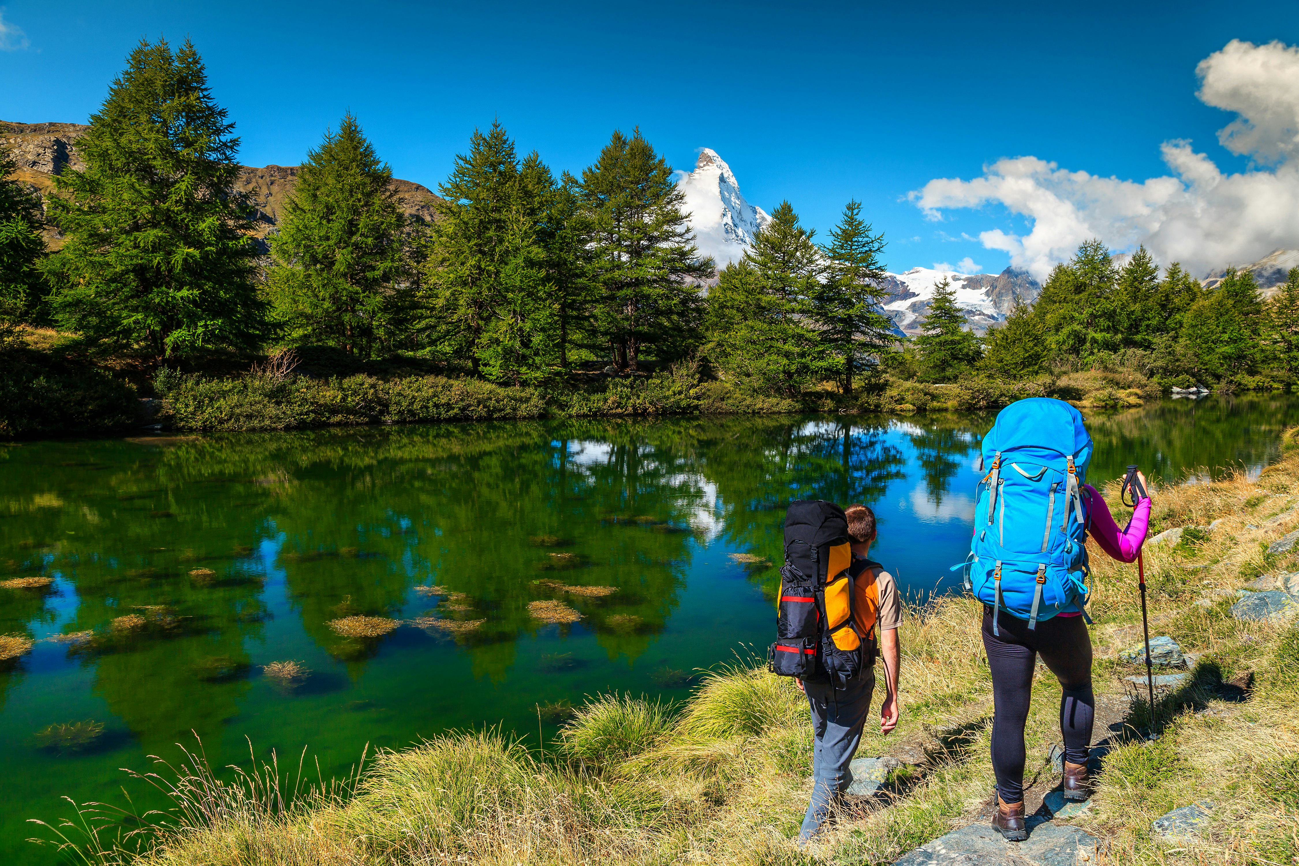 Two hikers hike Zermatt's Grindjisee Alpine Lake in Switzerland with the peak of Matterhorn mountain in the background