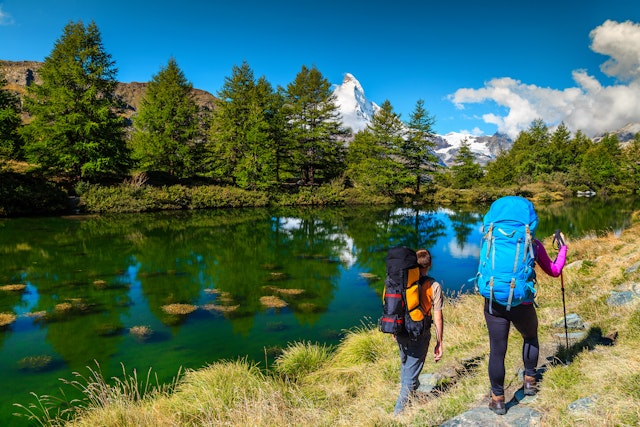 Two hikers hike Zermatt's Grindjisee Alpine Lake in Switzerland with the peak of Matterhorn mountain in the background