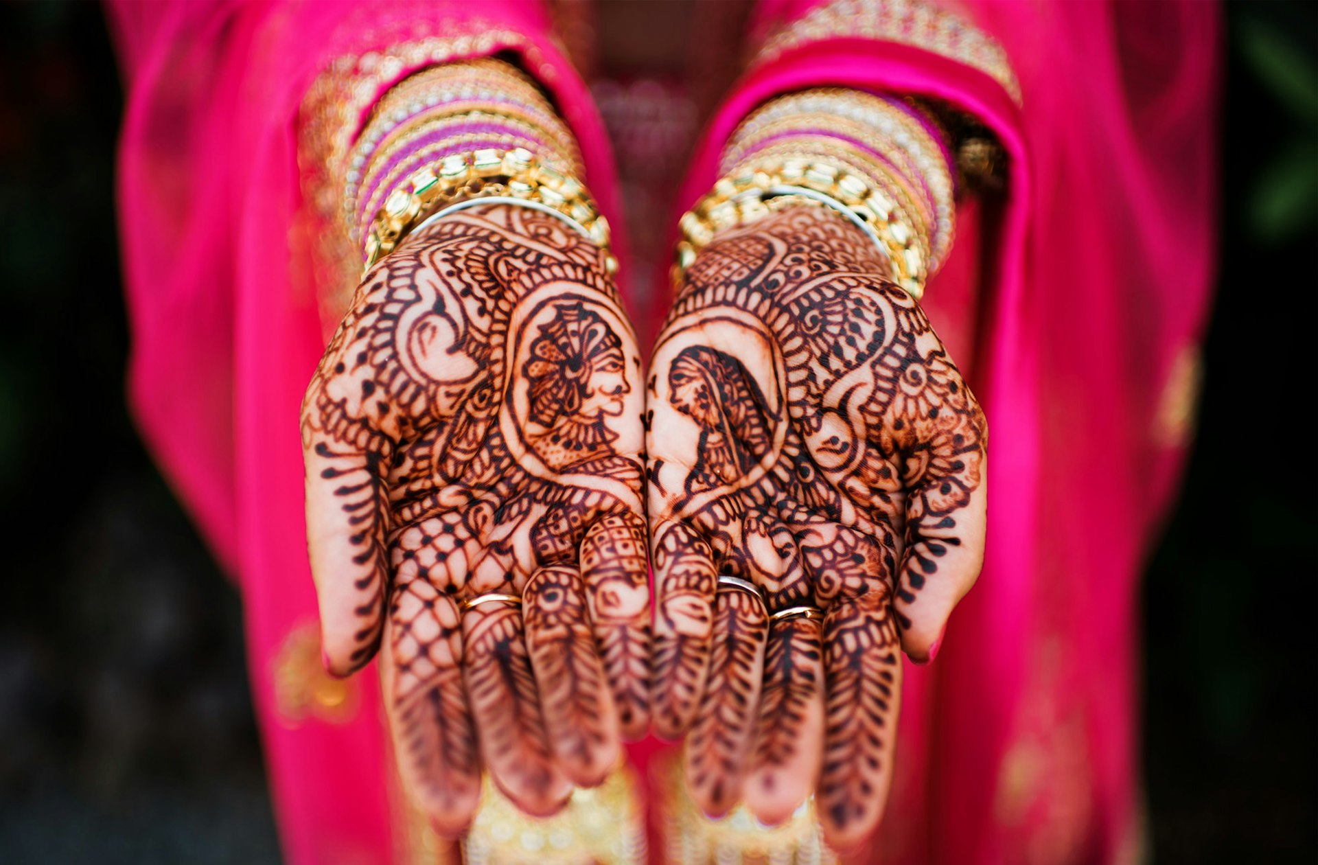 A bride in a bright pink sari shows off her henna designs on her hands