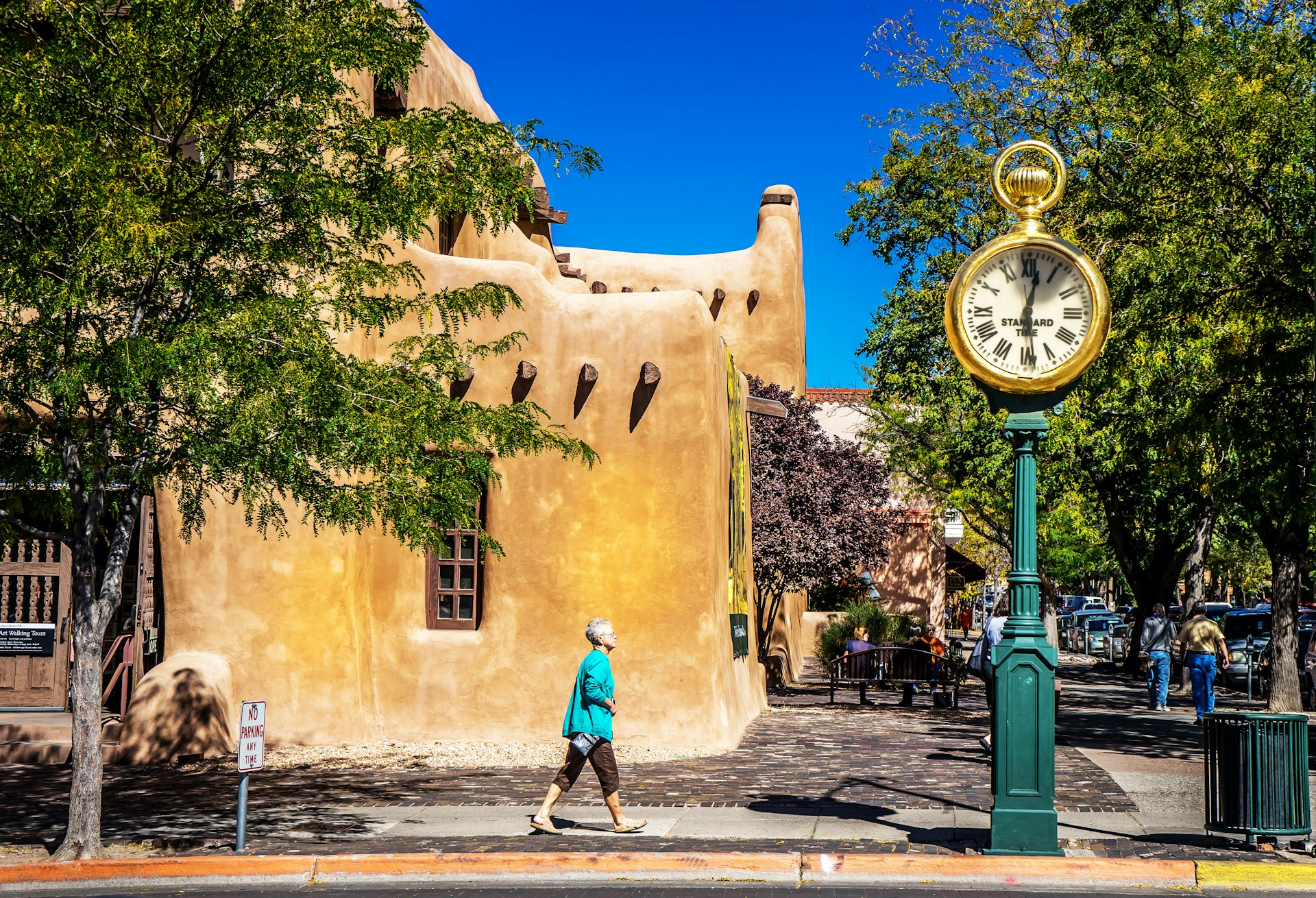 A woman walks by a tall clock on a street in a market in Santa Fe, New Mexico 