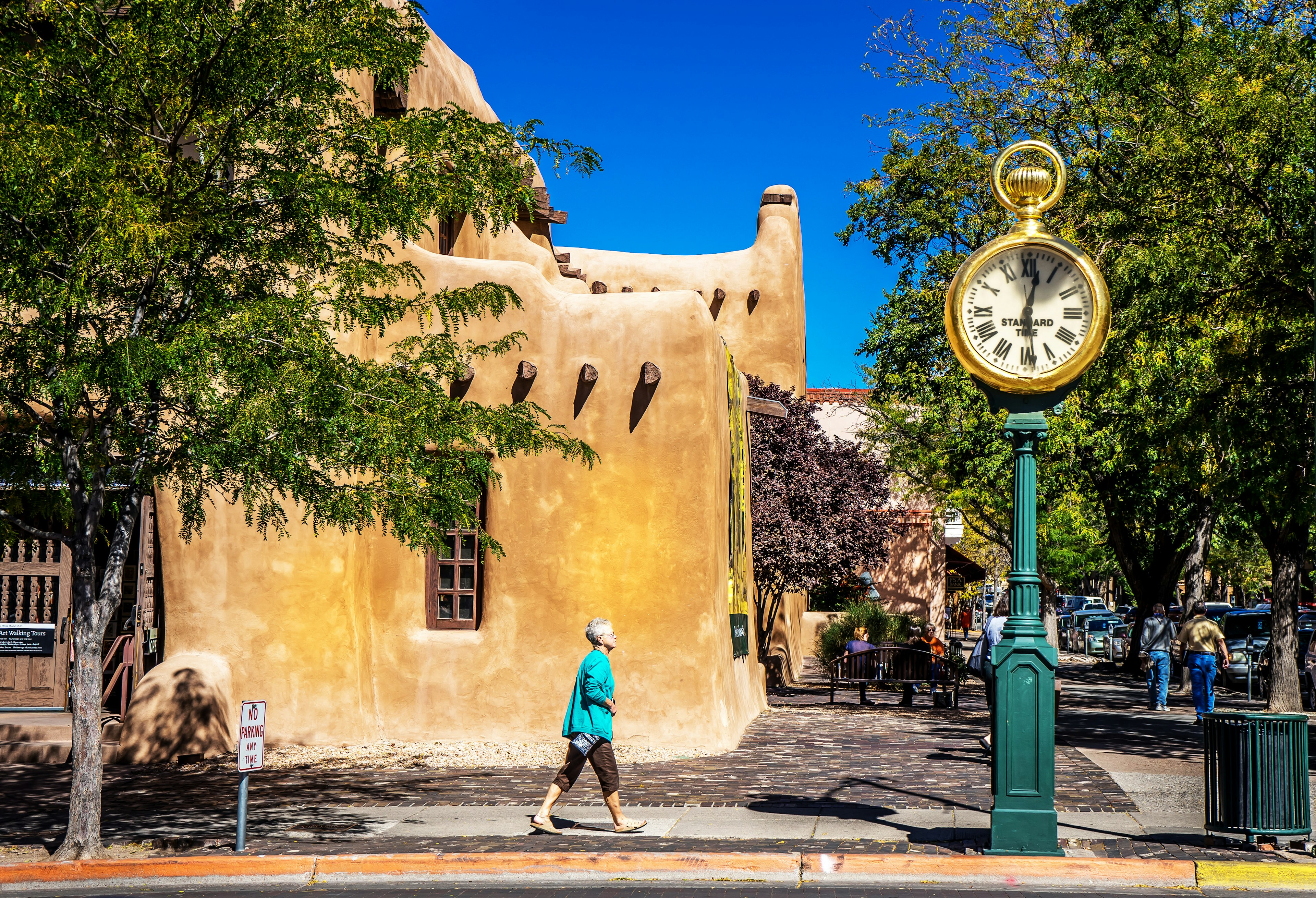 A woman walks along a road in Santa Fe, with one of the characteristic copper-hued buildings behind her.