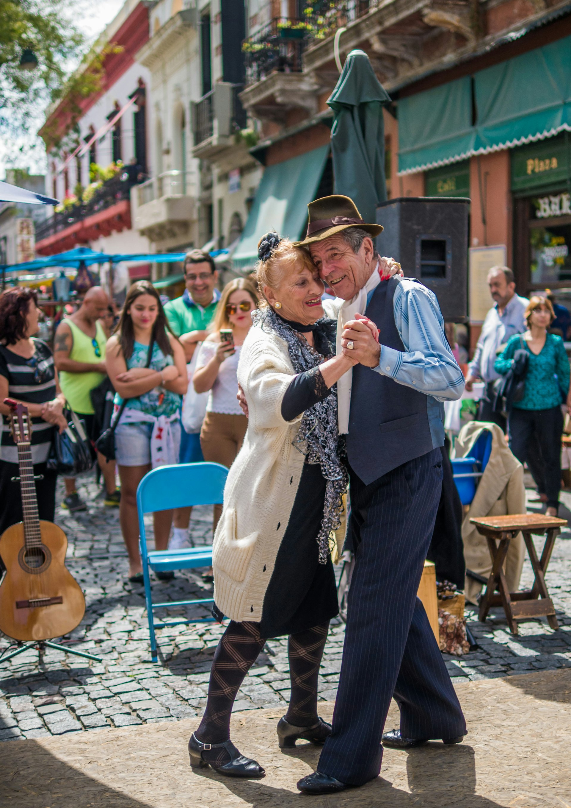 A pair of elderly tango dancers perform on a busy street with many smiling people watching on