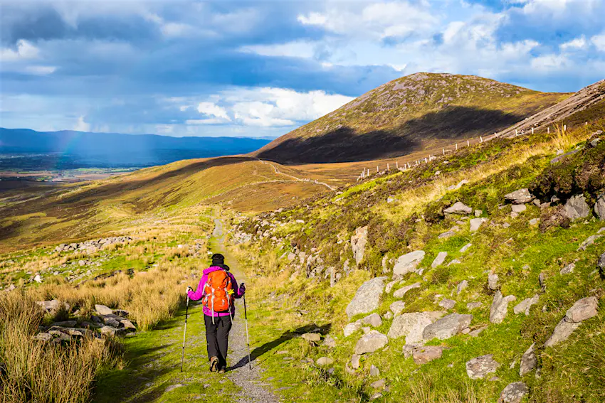 shutterstockRF_426445915.jpg A woman hikes in the mountains in Ireland with rain and rainbow in the distance, Macgillycuddy's Reeks
