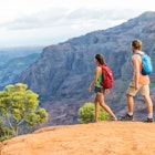 Hikers couple hiking in mountains landscape. Woman and man walking on hike in Waimea Canyon State Park, Kauai, Hawaii, USA. Looking at view happy enjoying healthy outdoor lifestyle.