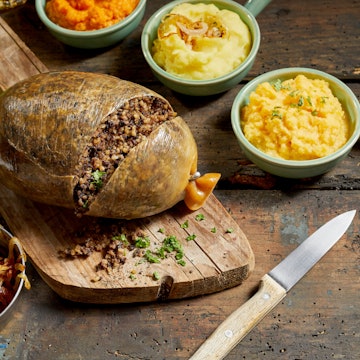 Traditional haggis meal for Robert Burns Supper, a Scottish tradition with cooked sliced haggis, neeps, tatties, onion and carrot. Served on a rustic table.
