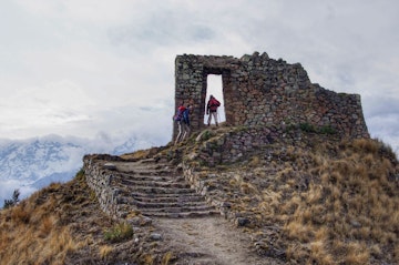 Two hikers walk up steps to a stone ruin in the Andes.