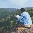 Asian man relaxing reading book on rocky cliff in mountains, Thailand