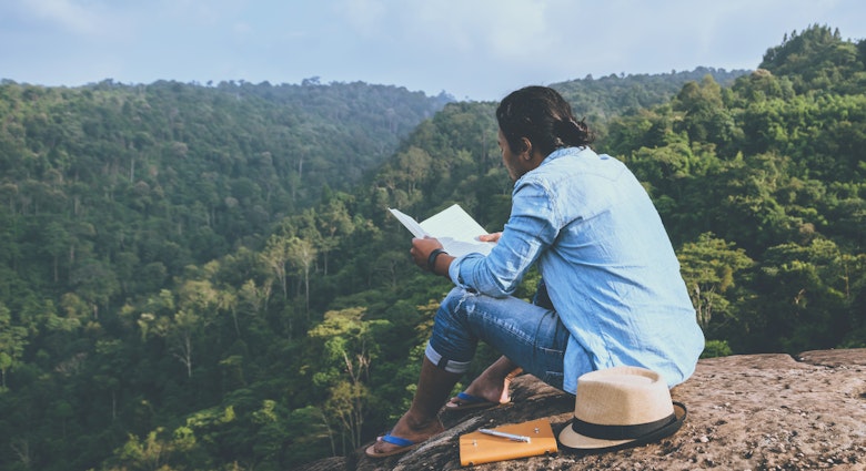 Asian man relaxing reading book on rocky cliff in mountains, Thailand