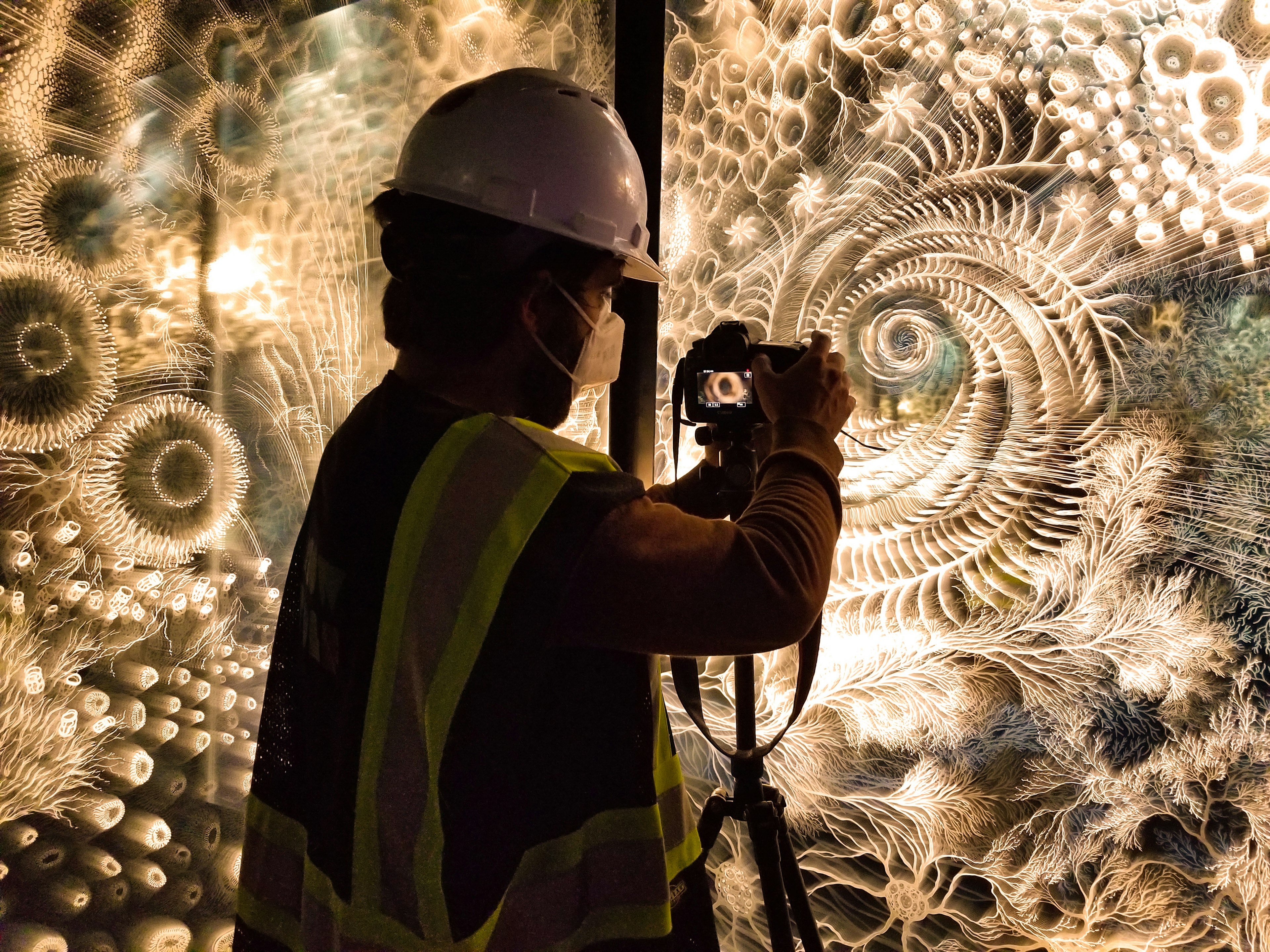 Claudia, wearing a hard hat and face masks, photographs her Pulse installation