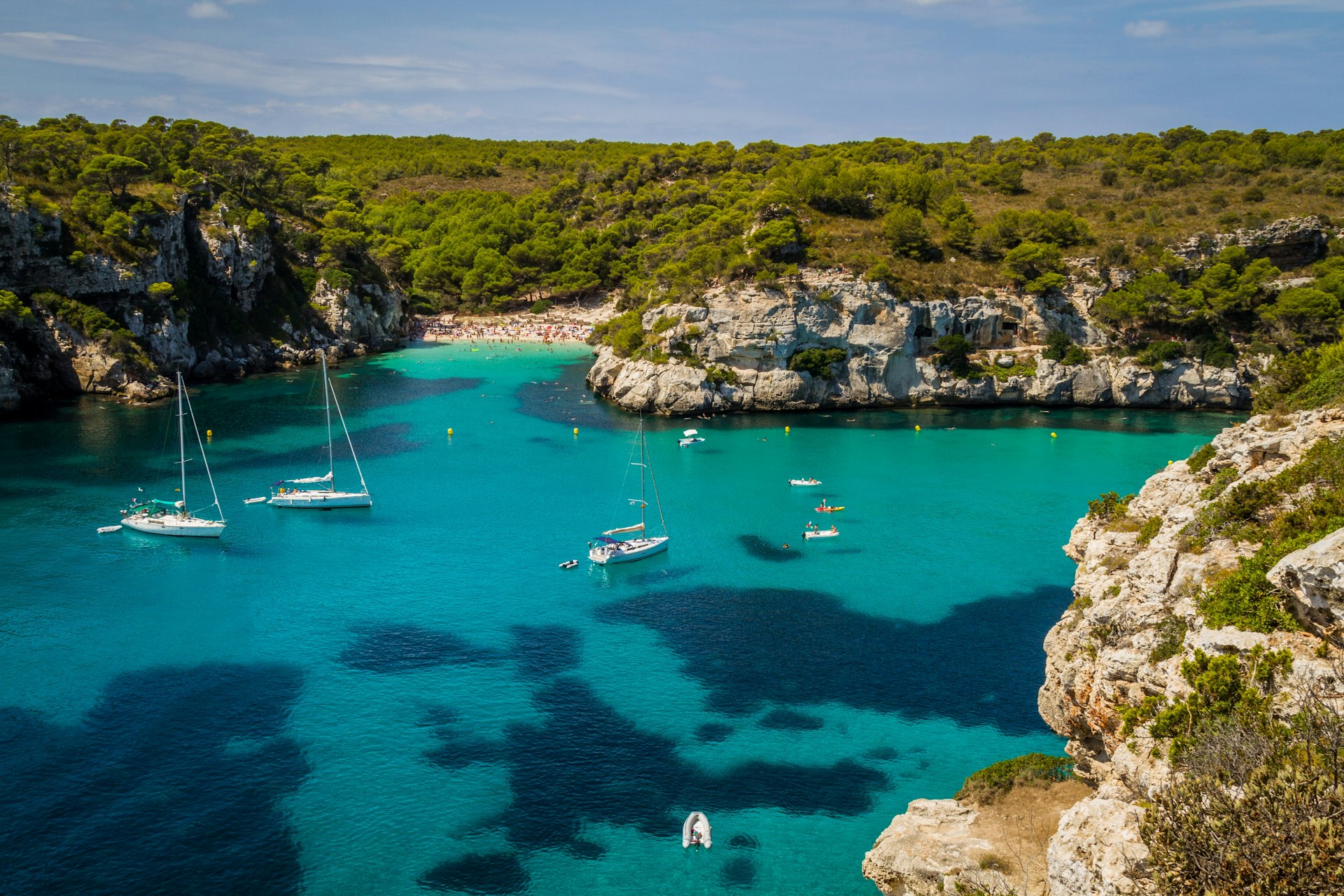 A turquoise bay of water meets a rocky coast. Several small white boats are moored there