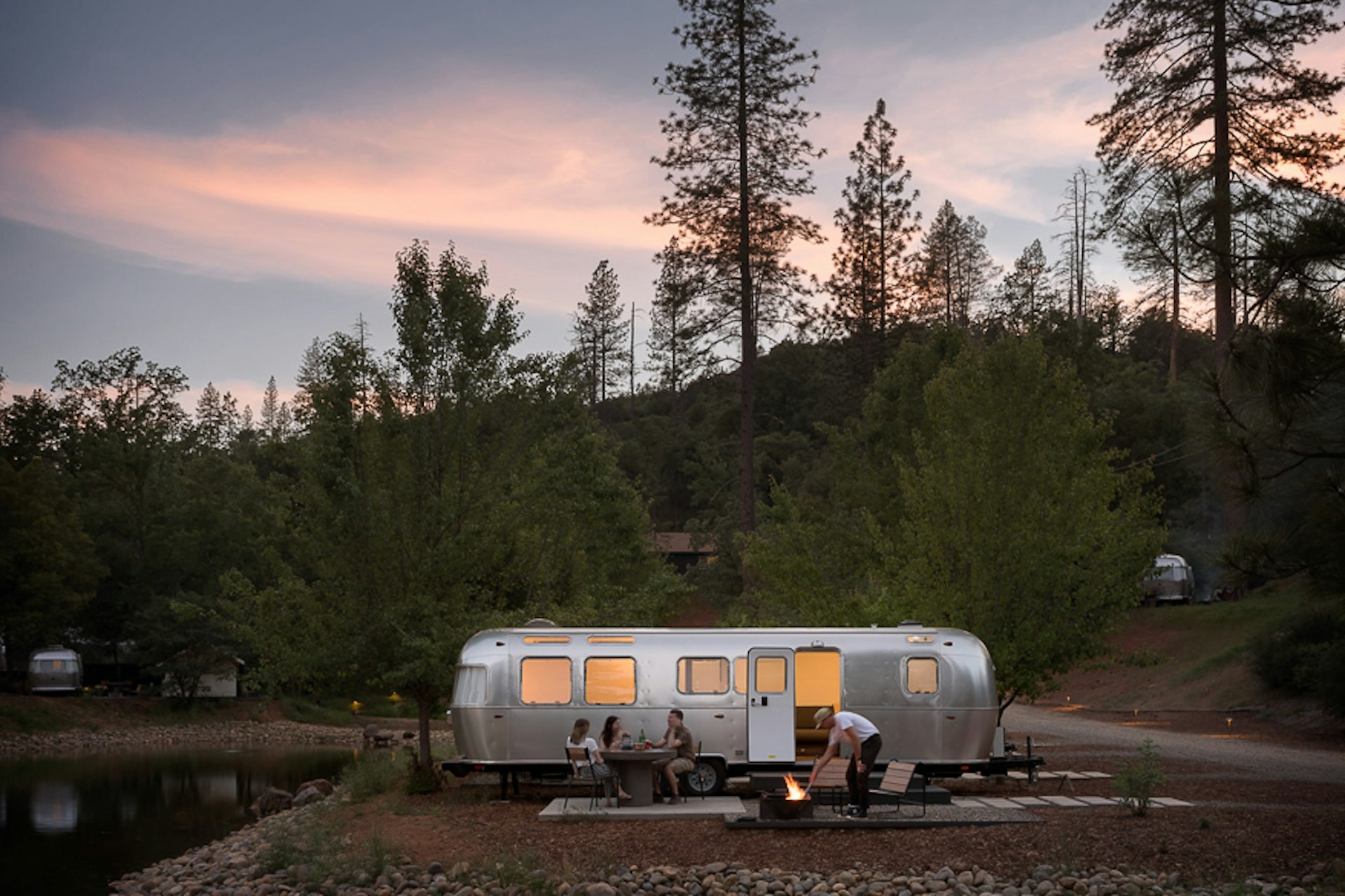 People outside an Airstream on a glamping site at a campfire