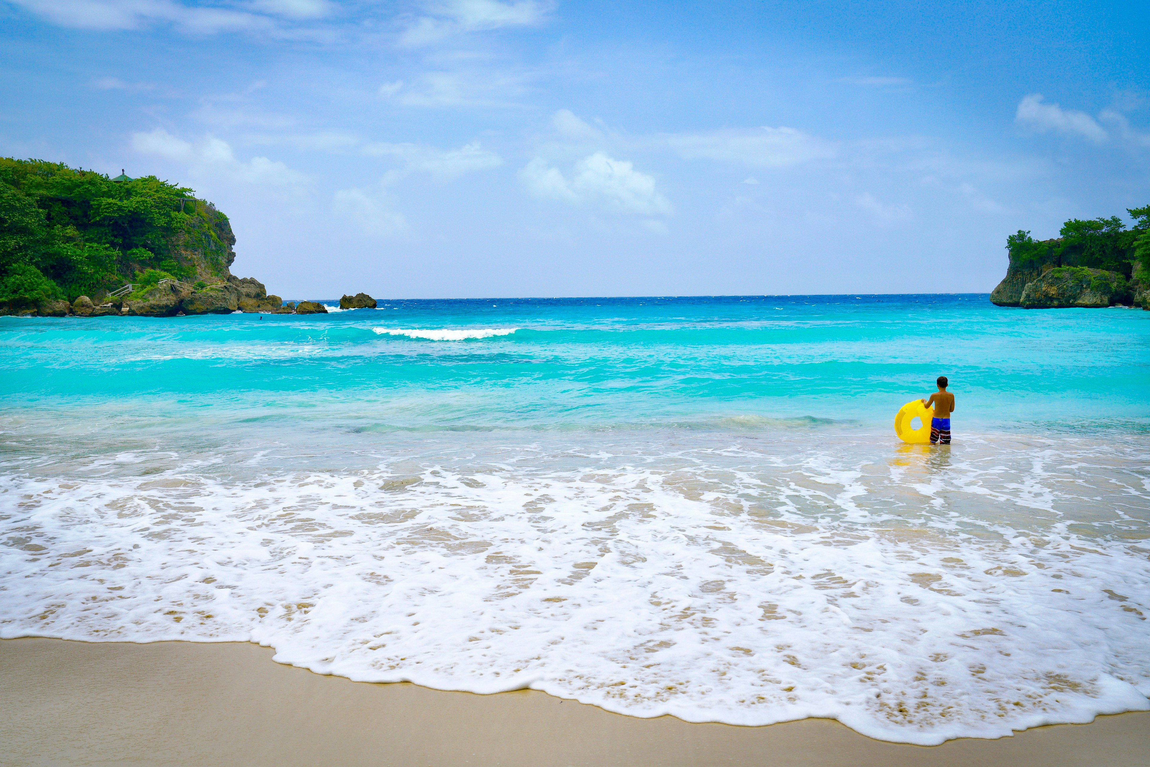 A man holding a yellow inflatable donut stands in knee-high water at Boston Bay Beach in Jamaica.