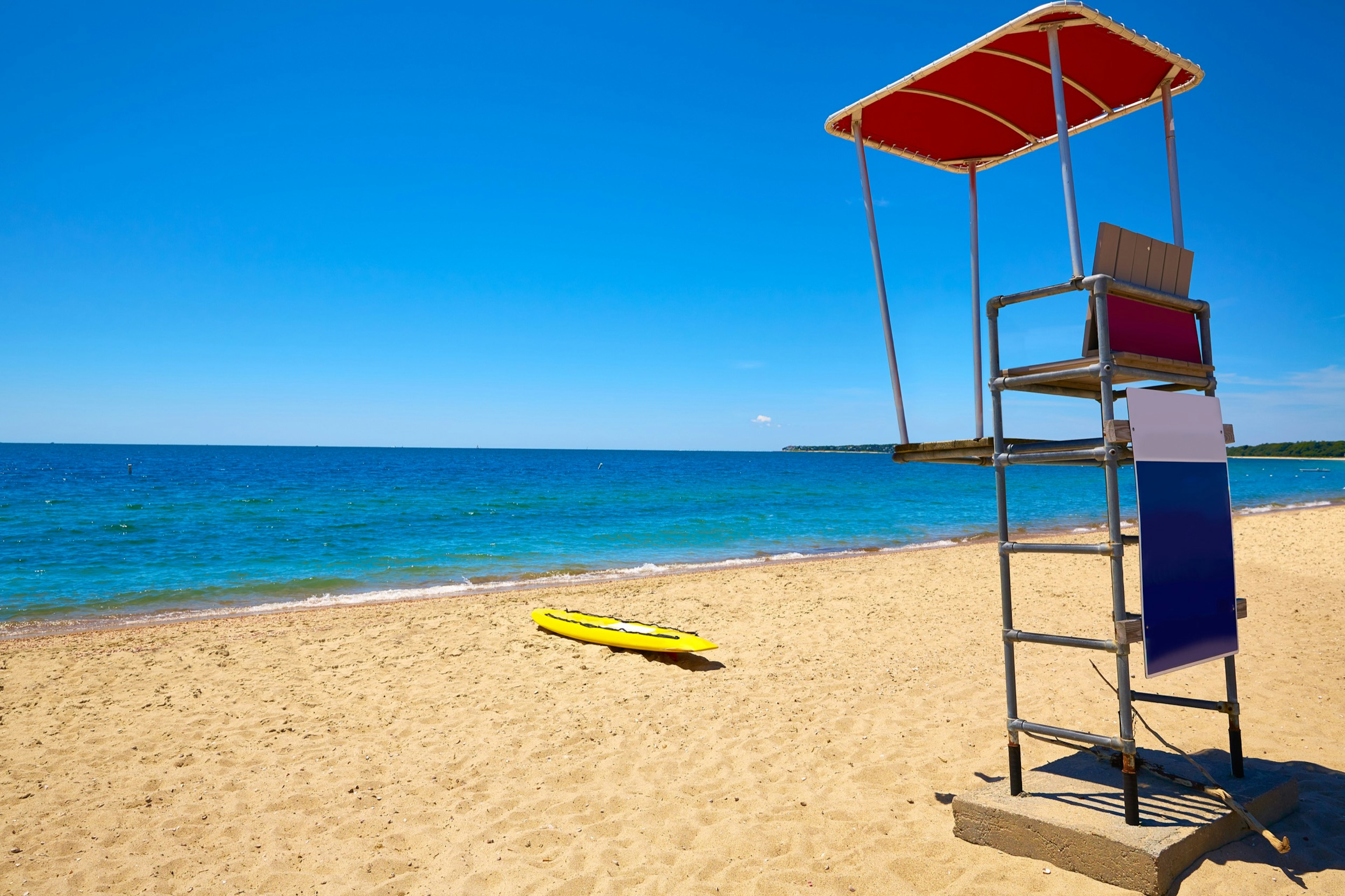 A lifeguard stand and a yellow surf board sit on the sand in front of the ocean at Craigville Beach